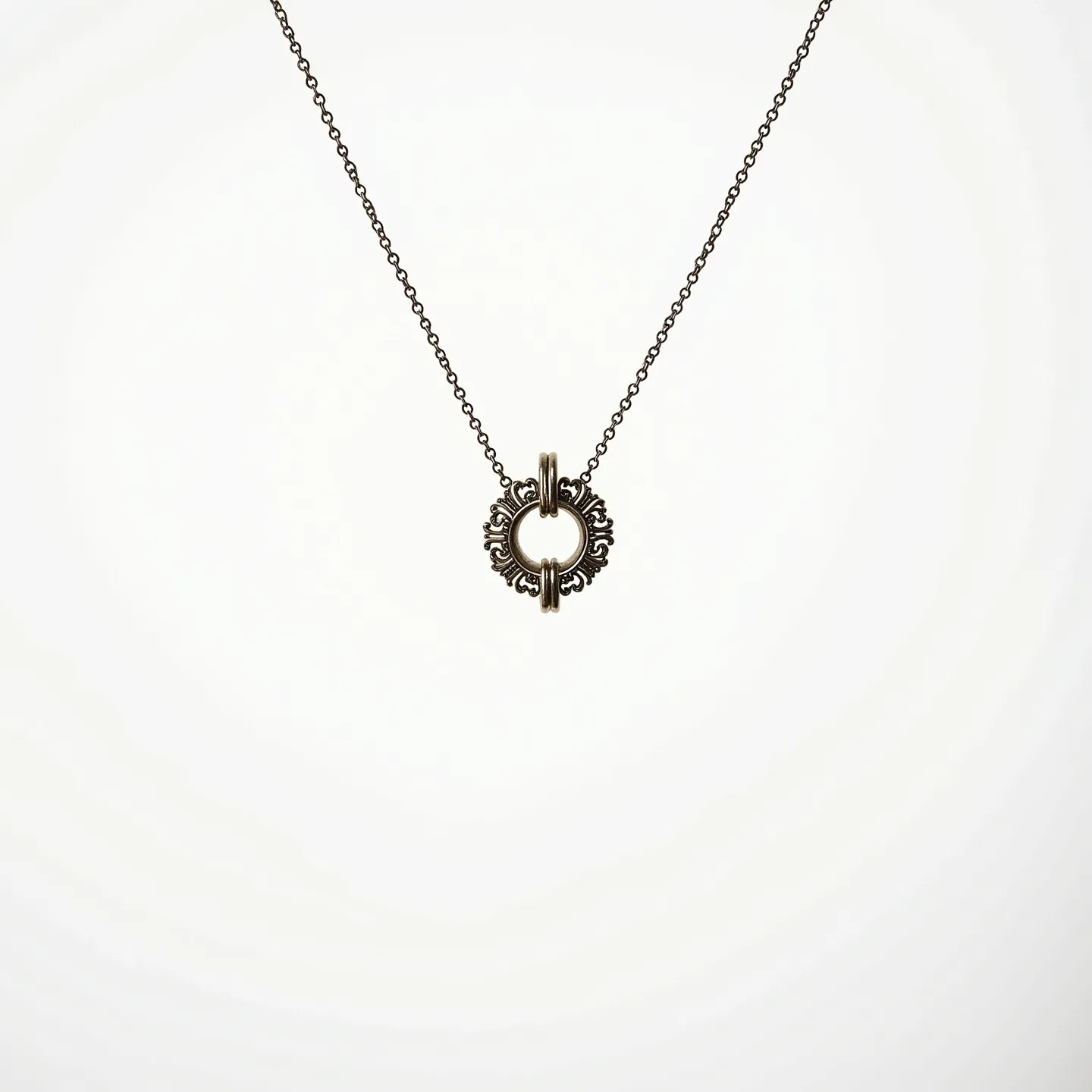 This ring necklace features a delicate chain that supports an intricately designed ring pendant, which appears to be made of metal. The pendant is circular with ornate detailing, giving it a vintage or antique look. The chain is composed of small, evenly spaced links and connects seamlessly to the pendant, likely using a simple jump ring for attachment. There are no visible gems or stones on the necklace, and the pendant takes center stage with its detailed craftsmanship. The necklace employs a standard clasp, possibly a lobster clasp, for easy fastening.