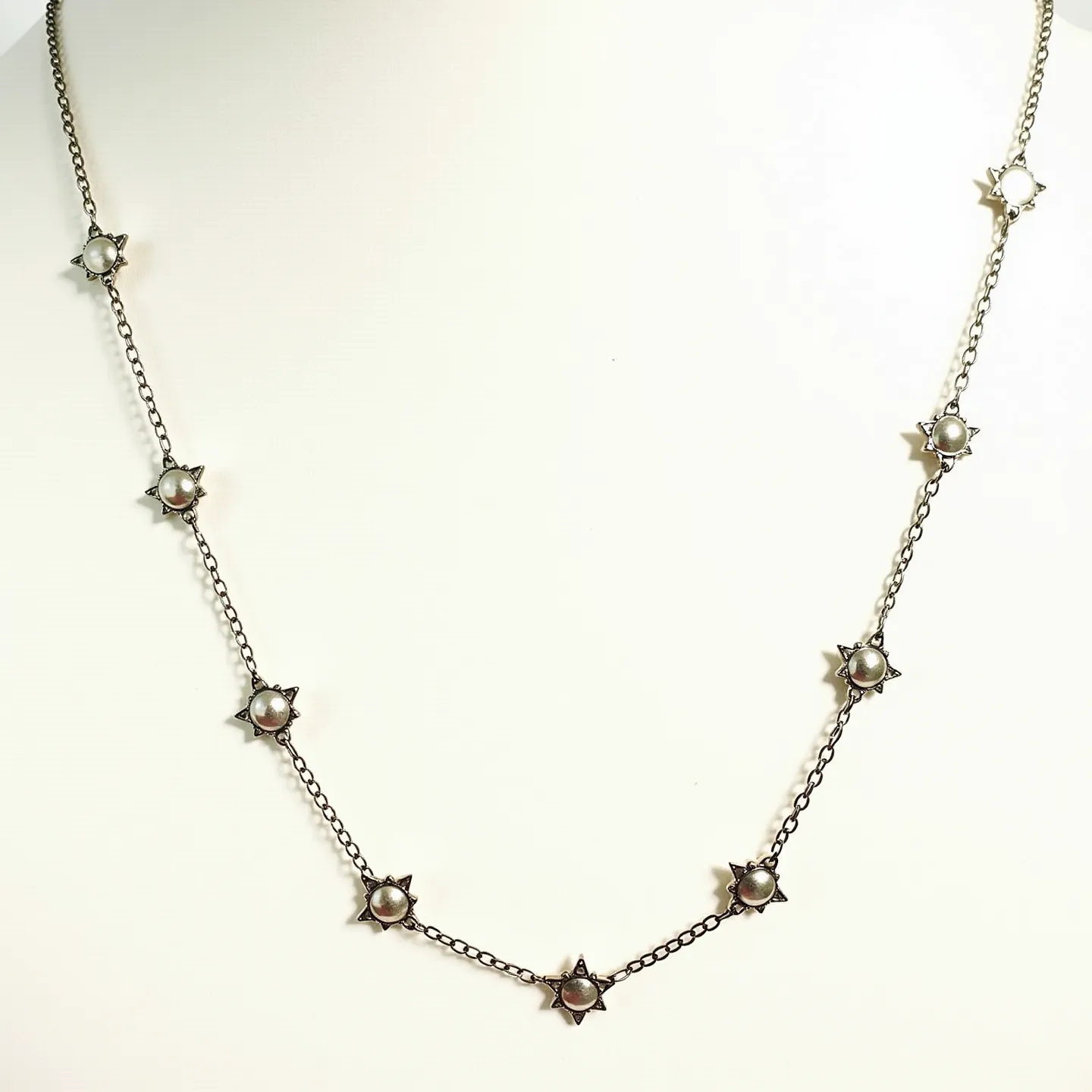 This rolo chain necklace features a series of equally spaced star-shaped settings, each centered with a pearl-like gemstone. The chain and star settings appear to be crafted from metal consistent with silver tones, lending a delicate and intricate design. The pearls provide a classic and elegant contrast to the metallic elements, enhancing the necklace's aesthetic appeal. The stars are evenly distributed along the length of the chain, offering a symmetrical and balanced visual effect. The necklace is completed with a clasp, which is likely a standard spring ring or lobster claw, aiding in a secure and functional closure.