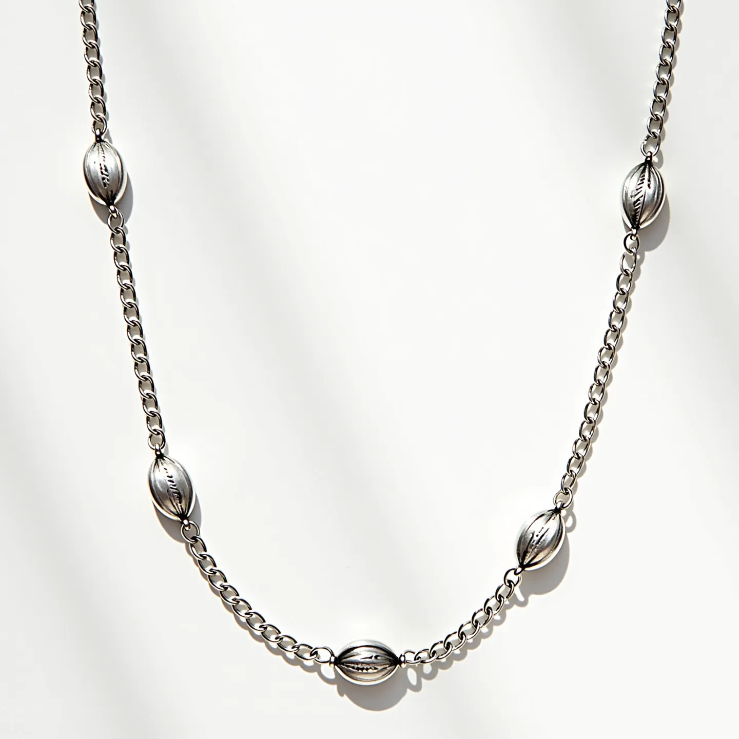 This rolo chain necklace is crafted from a metallic material, featuring smooth, circular links characteristic of the rolo style. Interspersed along the chain are polished, oval-shaped metallic beads that add a decorative element. The necklace does not appear to include any gemstones, focusing instead on the sleek, reflective surface of the metal. Each bead is uniformly spaced, suggesting a design that emphasizes symmetry and balance. The necklace likely includes a standard clasp mechanism to secure it, although it is not visible in the image provided.