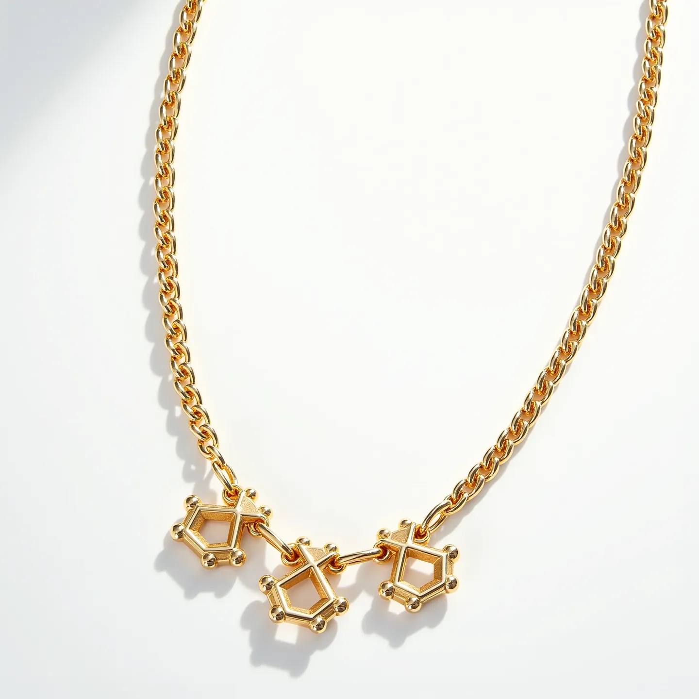 This rolo chain necklace is crafted from a polished gold-tone metal, featuring a series of evenly sized, circular links that form its chain. Suspended from the chain are three geometric pendants, each resembling a pentagon with five vertex points, adding a modern and artistic flair. The necklace showcases a sleek, minimalist design, allowing the unique shape of the pendants to stand out prominently. The clasp appears to be a simple and secure closure, ensuring ease of wear. The design is sophisticated and elegant, making it a striking accessory.