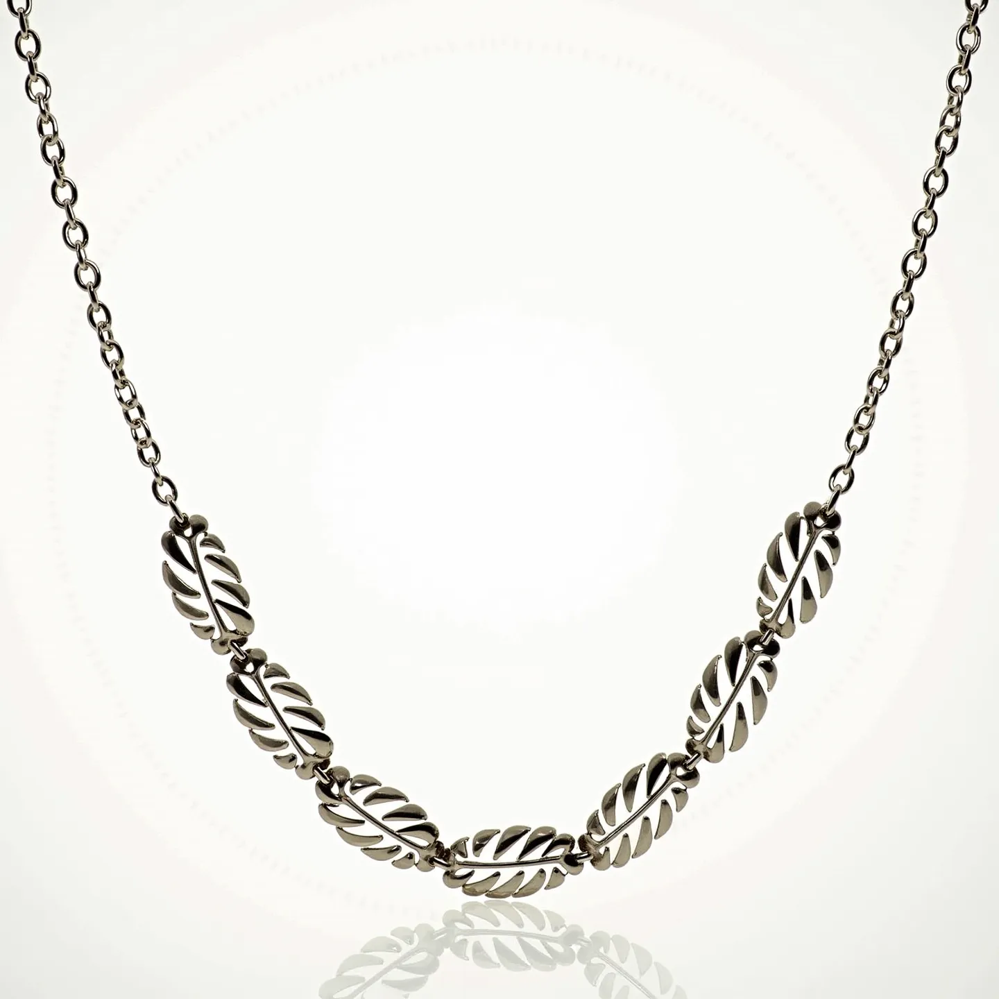 This rolo chain necklace features a series of intricately designed links in a polished metal, likely silver or white gold, giving it a sleek and refined appearance. Each link showcases a decorative leaf-like design that adds a touch of elegance to the overall piece. The chain appears to be crafted from round interconnected links, providing a balanced yet striking aesthetic. The necklace does not feature any gemstones, focusing on the detailed metalwork to make its statement. A secure lobster clasp is used to fasten the necklace, ensuring ease of use and wearability.