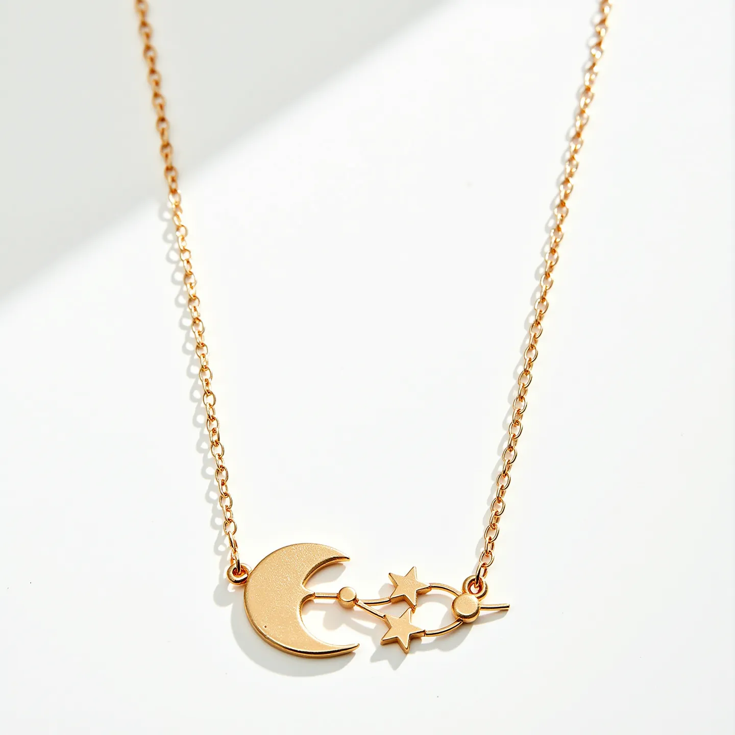 This rolo chain necklace features a delicate, gold-toned chain with evenly sized circular links, providing a refined and classic look. The necklace prominently displays a celestial-themed pendant, including a crescent moon and two stars, all crafted from the same gold-toned material, offering a cohesive and harmonious aesthetic. The pendant is intricately designed, with the stars connected to the moon by a linear bar, enhancing the piece's visual interest. It is likely secured with a simple clasp at the back, ensuring both security and ease of wear.