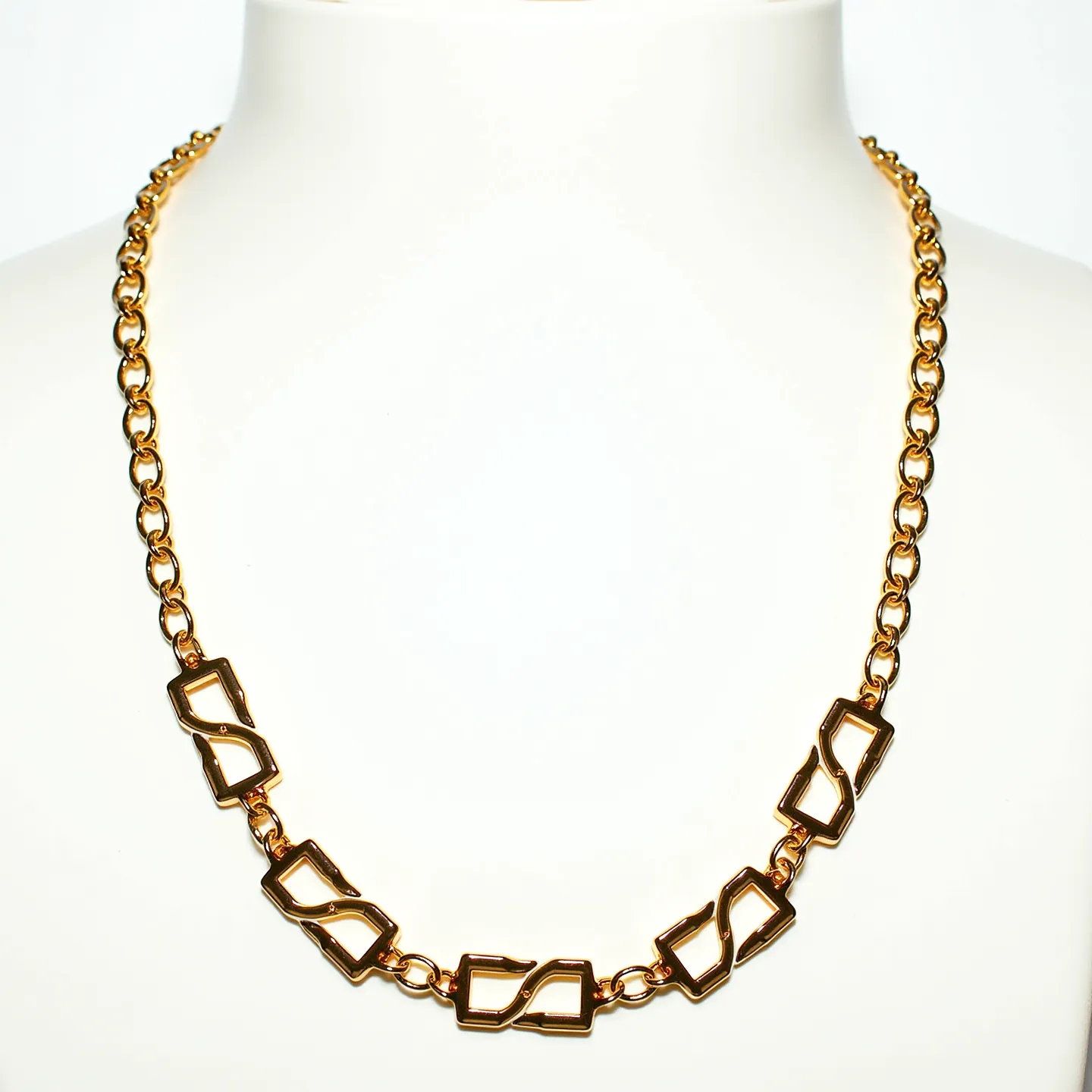 This rolo chain necklace is crafted from a gold-toned metal, featuring interlocking round links that provide a classic and elegant appearance. The necklace is adorned with uniquely designed rectangular geometric links in the center section, adding an artistic and modern flair to the overall design. The gold finish gives the necklace a luxurious sheen, making it suitable for both casual and formal wear. The necklace is equipped with a standard lobster clasp, ensuring a secure and convenient fasten. The combination of the traditional rolo chain with the contemporary geometric elements creates a balanced and stylish accessory.