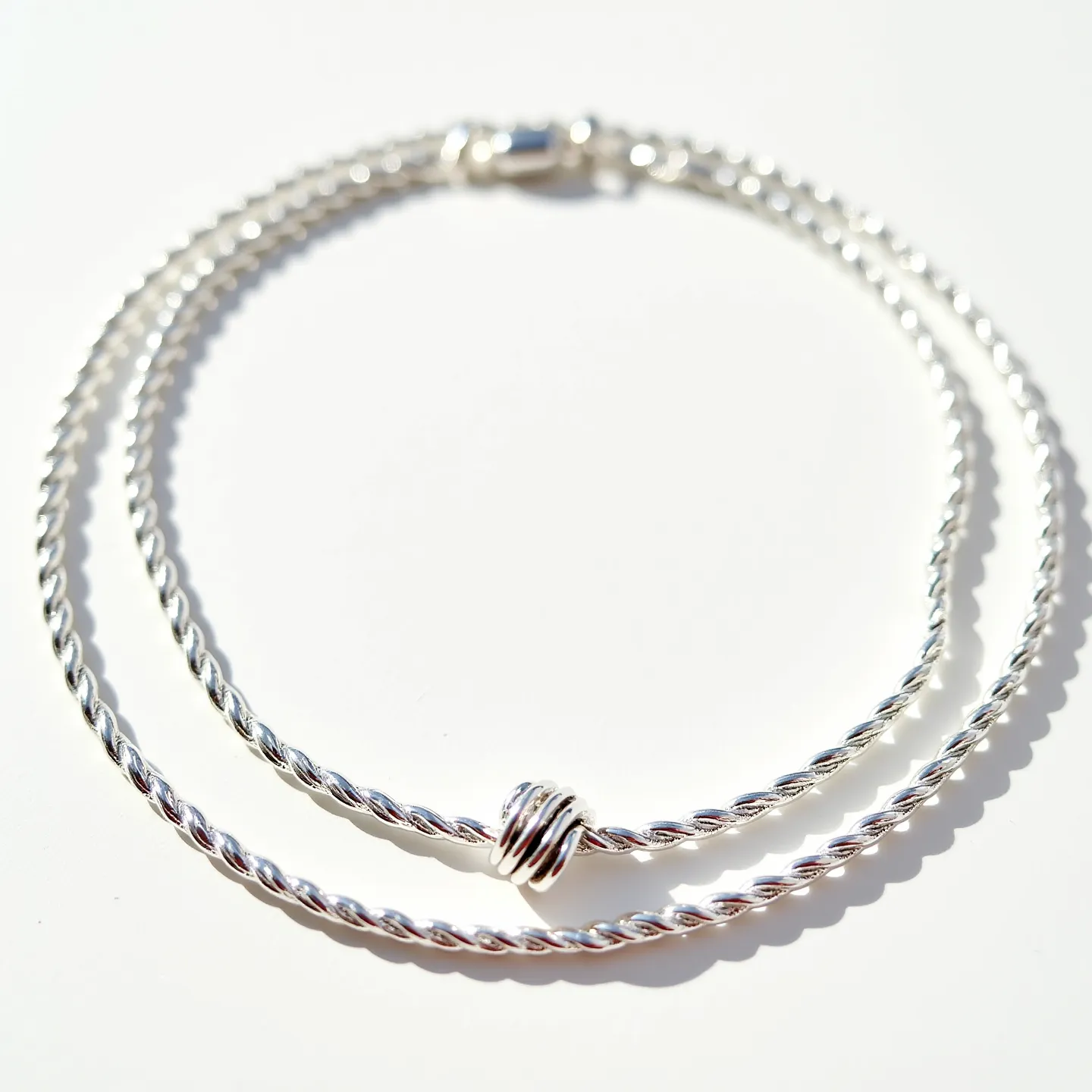 These rope chain features a classic twisted design crafted from a shiny silver-colored metal, exuding elegance and sophistication. At the center of the chain, there is a decorative bead, adding a touch of detail to the otherwise smooth and continuous design. The chain is equipped with a lobster clasp, ensuring secure fastening and easy wearability. The polished finish of the metal enhances its reflective qualities, making it a striking accessory suitable for various occasions.