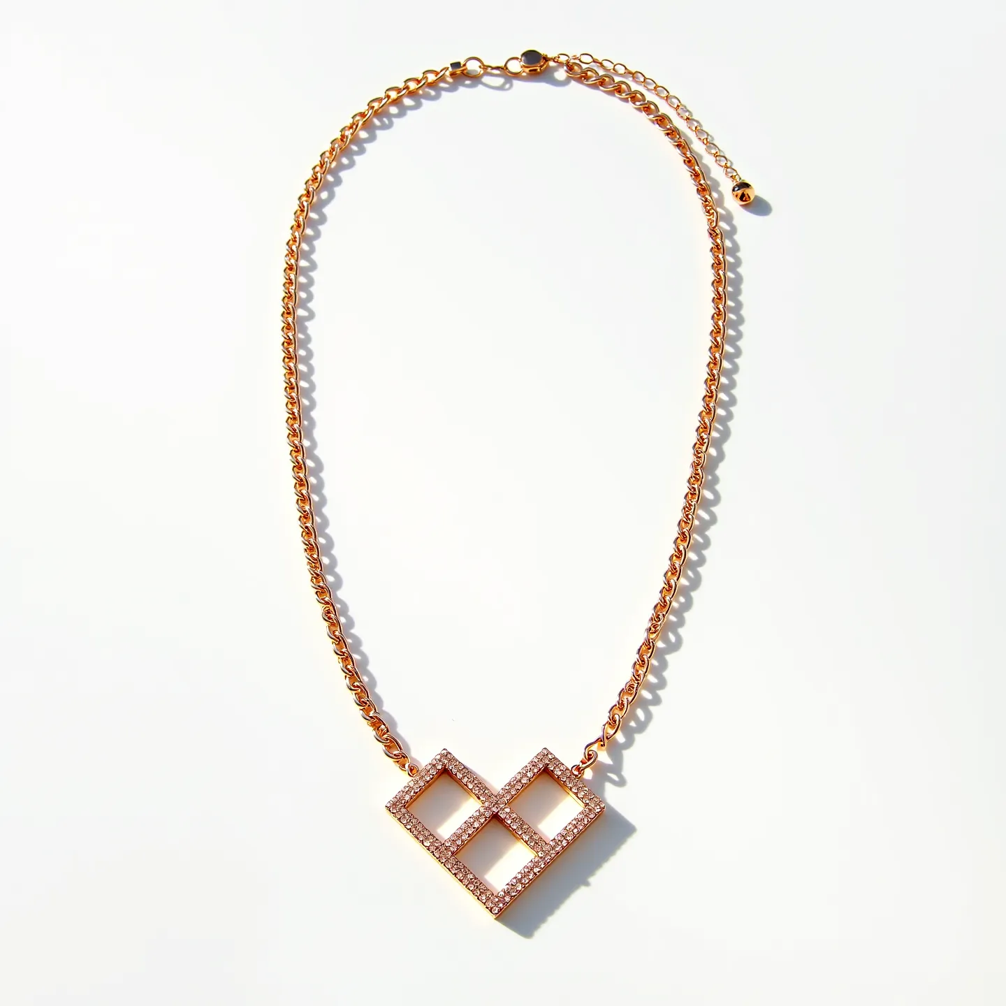 This rose gold necklace features a delicate chain crafted from rose gold metal, which provides a warm and elegant sheen. The centerpiece of the necklace is a geometric pendant shaped like a stylized, angular heart, incorporating a design of interconnected squares. The pendant is adorned with small, sparkling gems that are likely diamonds or simulated diamonds, set in a pavé setting that enhances their brilliance and creates a continuous shimmer across the surface. The necklace is secured with a lobster clasp, allowing for a secure attachment, and has an adjustable length with an extender chain, ending with a small spherical ornament for added detail.