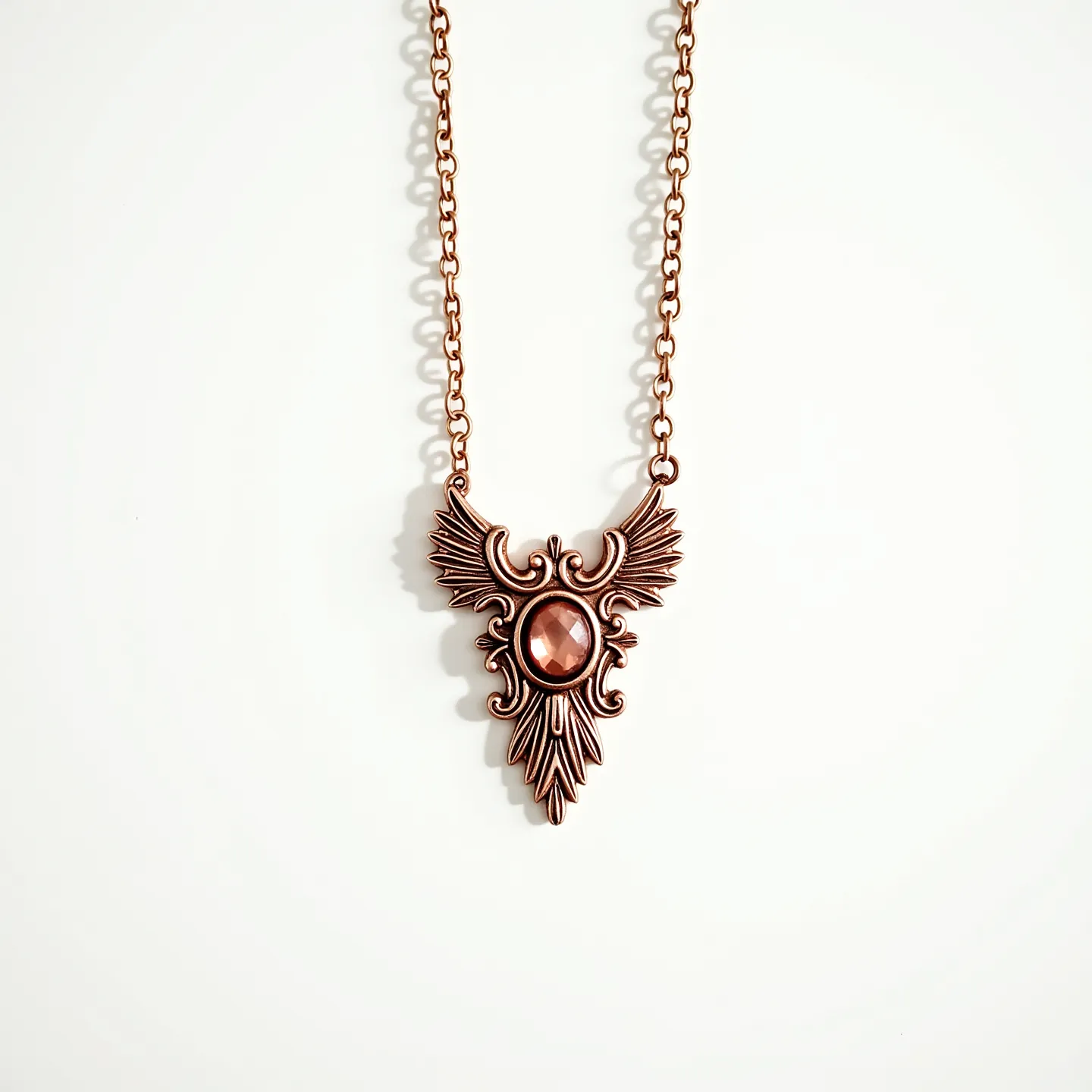 This rose gold necklace features a beautifully ornate pendant with intricate detailing that resembles wings and scrolls. At the center of the pendant is a faceted gemstone, likely a rose-colored quartz or similar, set into an elegant bezel setting that enhances its reflective qualities. The chain is composed of interlocking oval links, providing a sturdy and complementary framework for the pendant. The necklace is secured with a lobster clasp, ensuring both practicality and ease of wear. The overall design combines vintage elegance with a touch of modern sophistication.