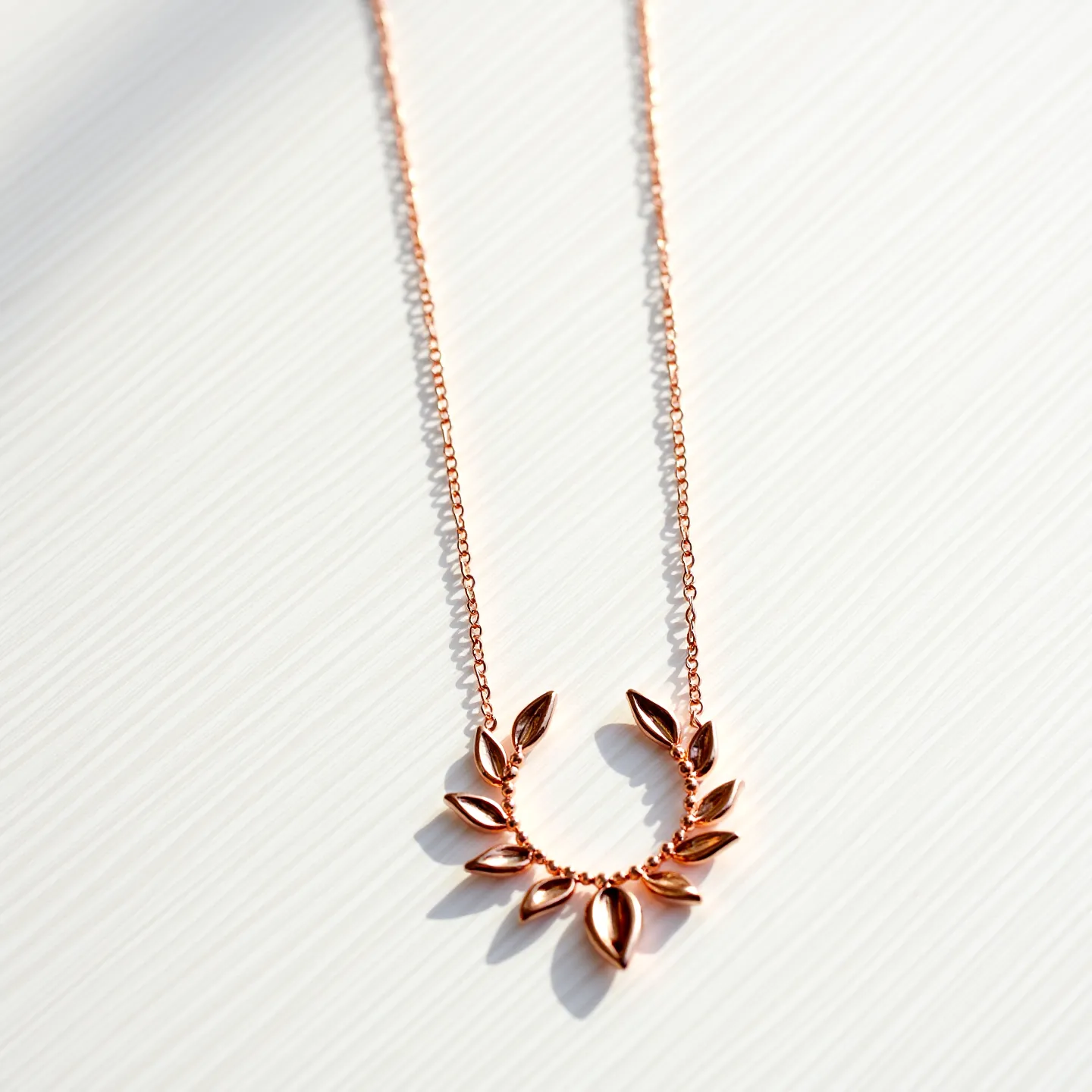 This rose gold necklace features a delicate chain with a central pendant designed in a circular shape adorned with small, leaf-like motifs. The rose gold gives the piece a warm, pinkish hue, contributing to its elegant and timeless aesthetic. The necklace is crafted from rose gold metal but does not feature any additional gems or stones. The design is prominently formed with smooth, polished surfaces that catch and reflect light beautifully. Overall, the piece is a graceful addition to any jewelry collection, combining simplicity with subtle sophistication.