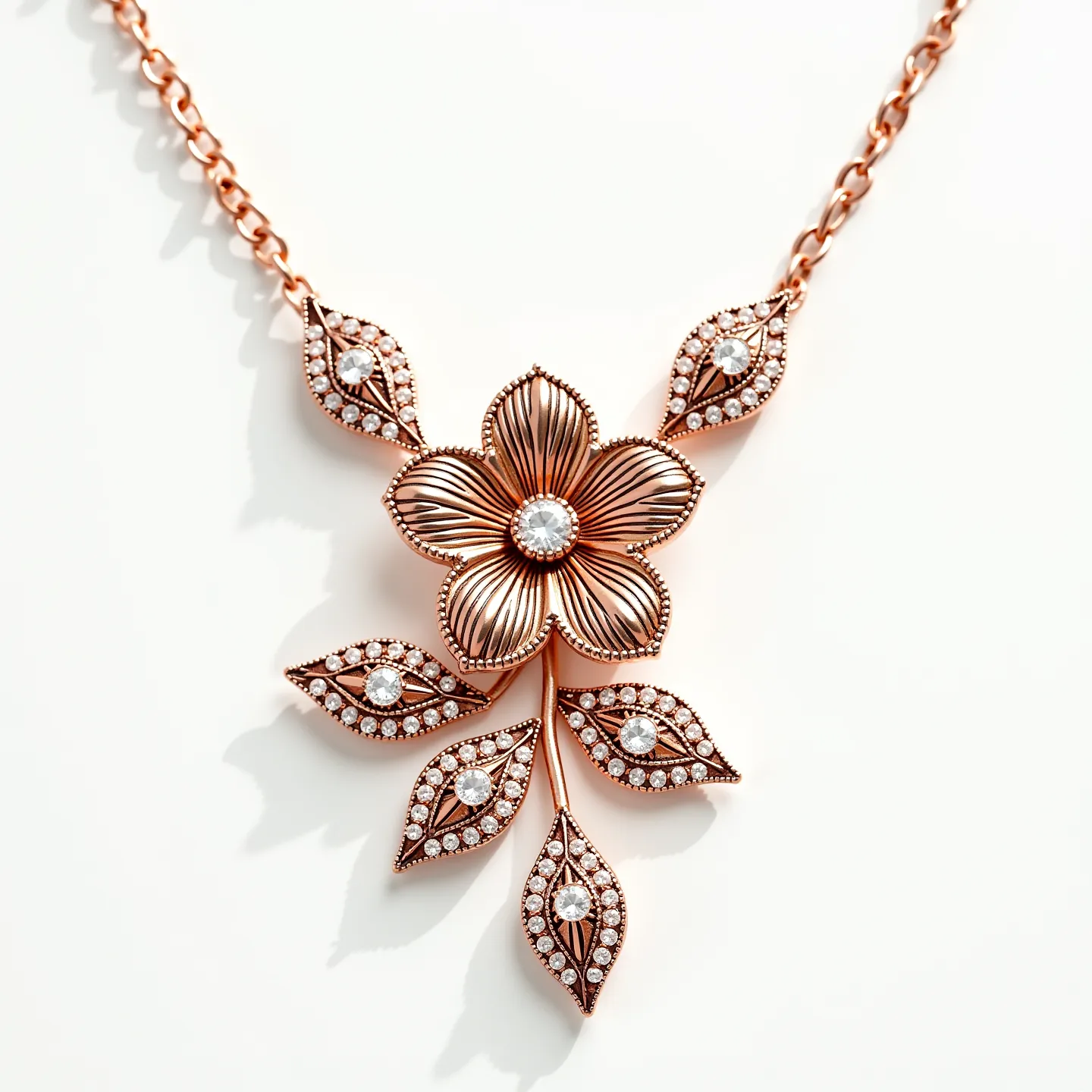 This rose gold necklace features an intricate floral design with a central flower comprised of delicately textured petals. At the heart of the flower is a round brilliant-cut gem set in a bezel setting, enhancing its sparkle and prominence. Surrounding the flower are ornate leaves adorned with smaller matching gems, also set in a bezel setting. The chain appears to be crafted from rose gold links that complement the pendant's elegant floral motif, and it is equipped with a traditional clasp for secure fastening. The overall design combines elegance with a touch of nature-inspired artistry.