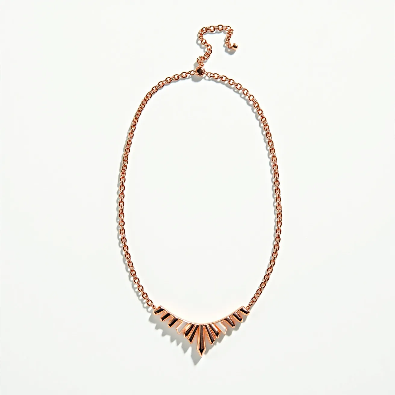 This rose gold necklace features a distinctive geometric design with a series of triangular elements arranged in a V-shaped pattern at the center. The necklace is crafted from rose gold-colored metal, giving it a warm, elegant appearance. It is comprised of a chain link that secures around the neck with an adjustable clasp, allowing for a tailored fit. The clean, angular lines of the geometric elements create a modern yet sophisticated look, making it suitable for various occasions.