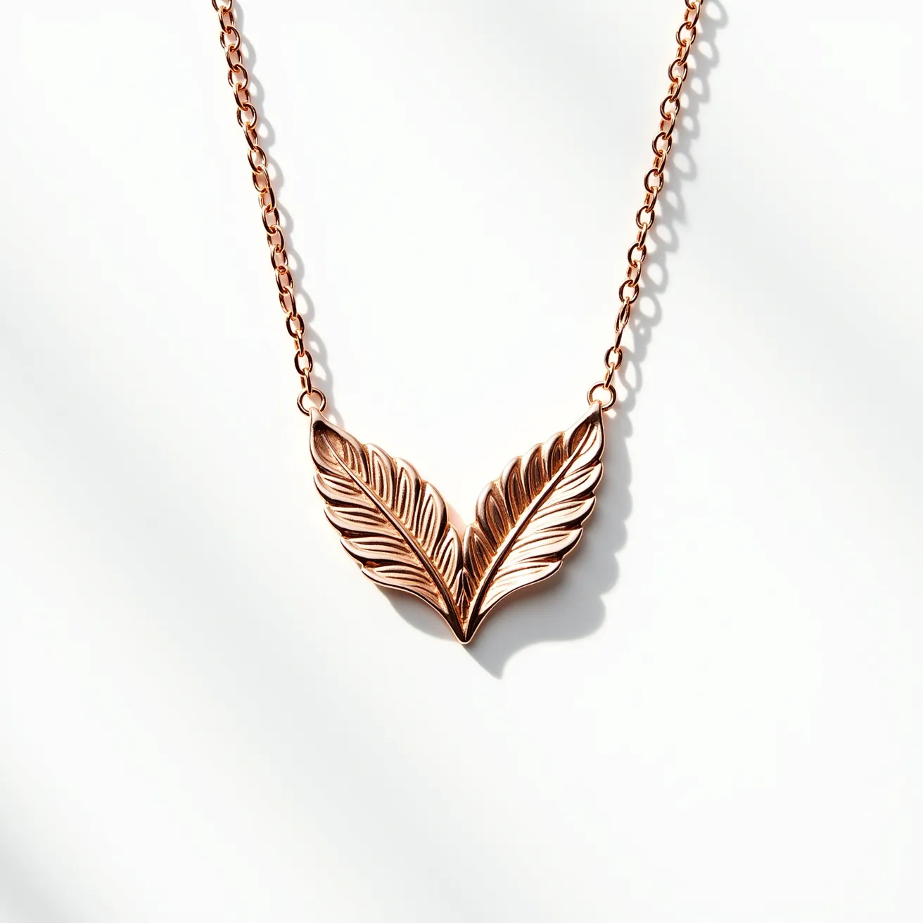 This rose gold necklace features a delicate chain with a striking pendant in the shape of stylized leaves. The leaves are crafted with detailed engraving, giving them a textured and lifelike appearance. The pendant is centrally connected to the chain, which appears to have a seamless attachment that complements the overall design. The rose gold material gives the necklace a warm and elegant hue, highlighting the intricate details of the leaves.