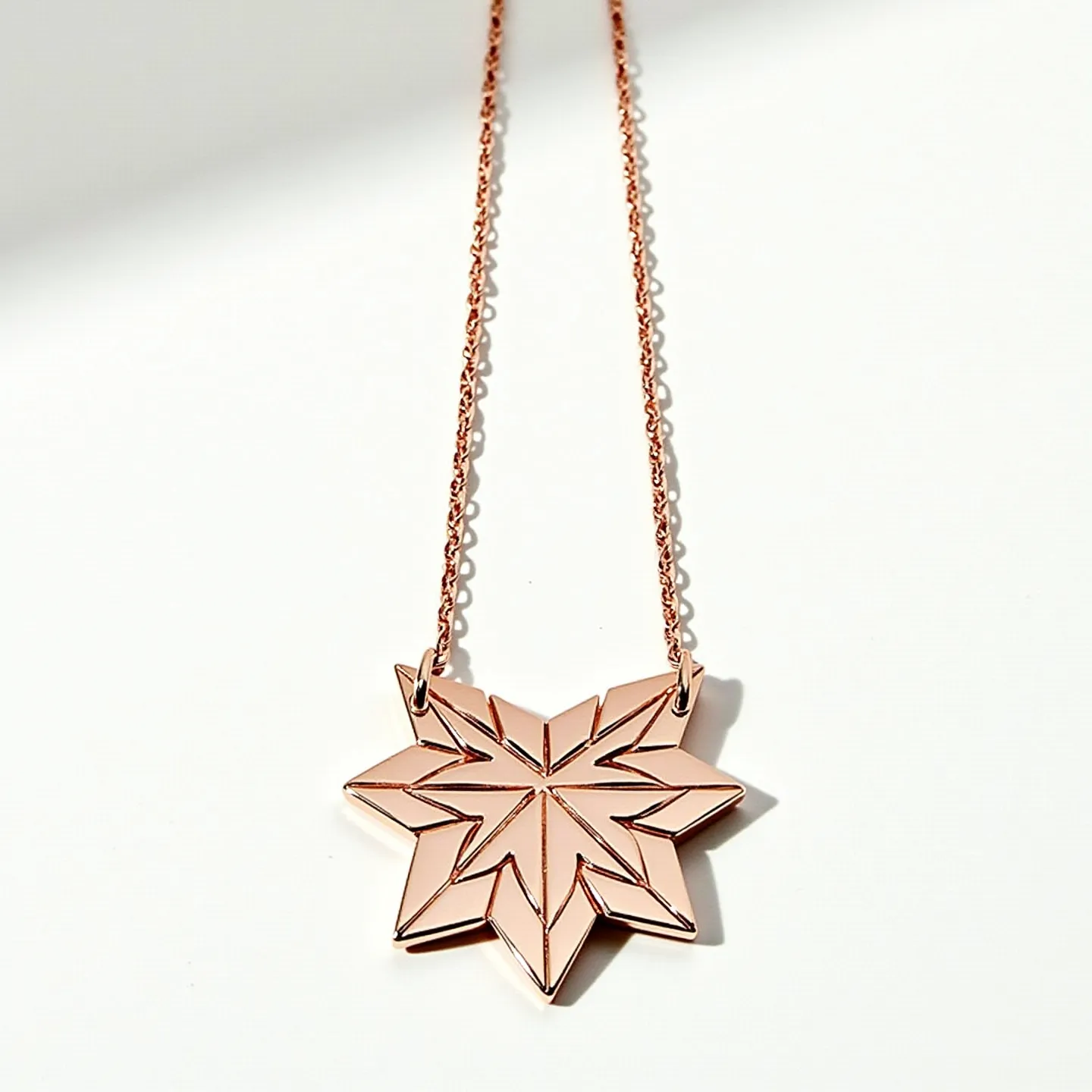 This rose gold necklace features a beautifully crafted geometric star-shaped pendant, showcasing an intricate pattern that draws attention to its elegant design. The pendant is seamlessly integrated into a delicate chain, also made from rose gold, which complements the pendant's polished surface. The necklace is likely secured with a discreet clasp that maintains the overall sophistication of the piece. The design exudes a modern yet timeless appeal, making it a versatile addition to any jewelry collection.