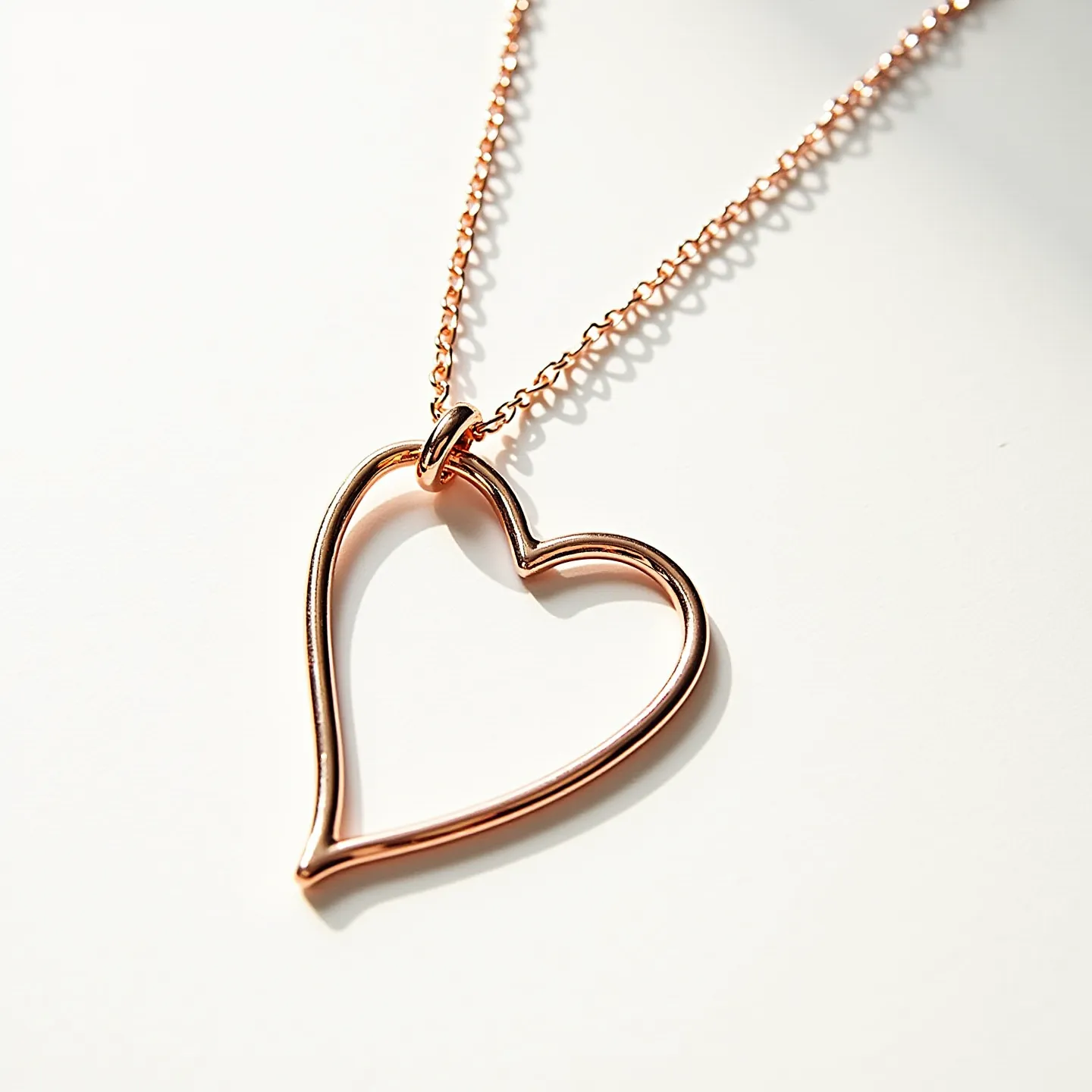 This rose gold necklace features a delicate heart-shaped pendant made of polished rose gold metal, showcasing a minimalist design. The heart pendant is attached to a matching rose gold chain, which is characterized by fine links that contribute to its elegant appearance. The necklace includes a simple loop through which the pendant is threaded, maintaining alignment and fluidity. The metal's warm hue enhances its romantic charm, making it a tasteful piece suitable for various occasions.