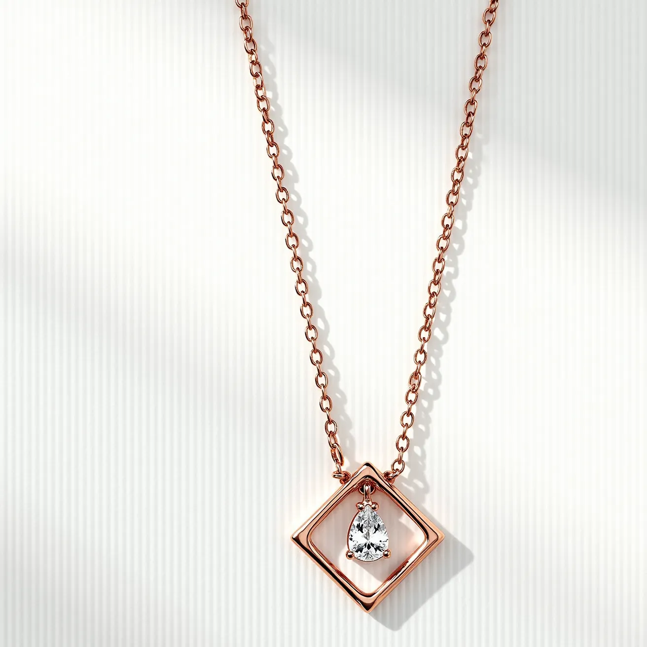 This rose gold necklace features a delicate chain with a geometric pendant element. Suspended within a rose gold square is a pear-shaped gemstone, skillfully prong-set to showcase its brilliance. The rose gold setting complements the stone's sparkle, adding a warm contrast that enhances the overall elegance of the piece. The necklace is secured with a simple yet functional clasp, ensuring both style and security.