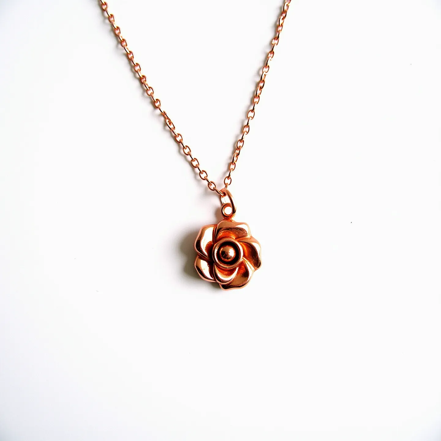 This rose necklace features a striking pendant shaped like a rose crafted from a rose gold-colored metal. The detailed design of the petals highlights the intricate craftsmanship of the piece. The pendant hangs from a delicate chain, which appears to be constructed from the same rose gold-colored material, creating a cohesive and elegant look. The chain links are small and evenly spaced, providing a subtle yet stylish texture to the necklace. The attachment of the pendant is seamless, ensuring that the rose is the focal point of this charming piece of jewelry.