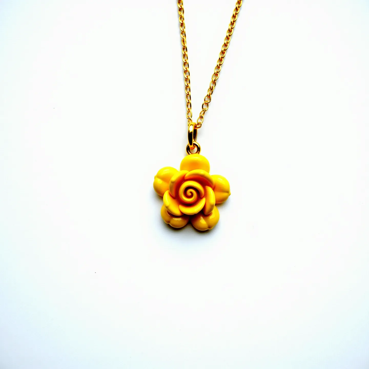 This rose necklace features a beautifully crafted yellow rose pendant made from a smooth, polished material, likely resin or a similar synthetic. The intricate design captures the delicate curves of rose petals with a central spiral detail. It hangs from a fine, gold-colored chain, which appears to be a simple cable chain, offering a classic and elegant look. The pendant is attached using a small, gold-tone bail that seamlessly matches the chain, ensuring a unified appearance. The necklace is designed with a cohesive aesthetic, emphasizing the vibrant and cheerful hue of the rose.