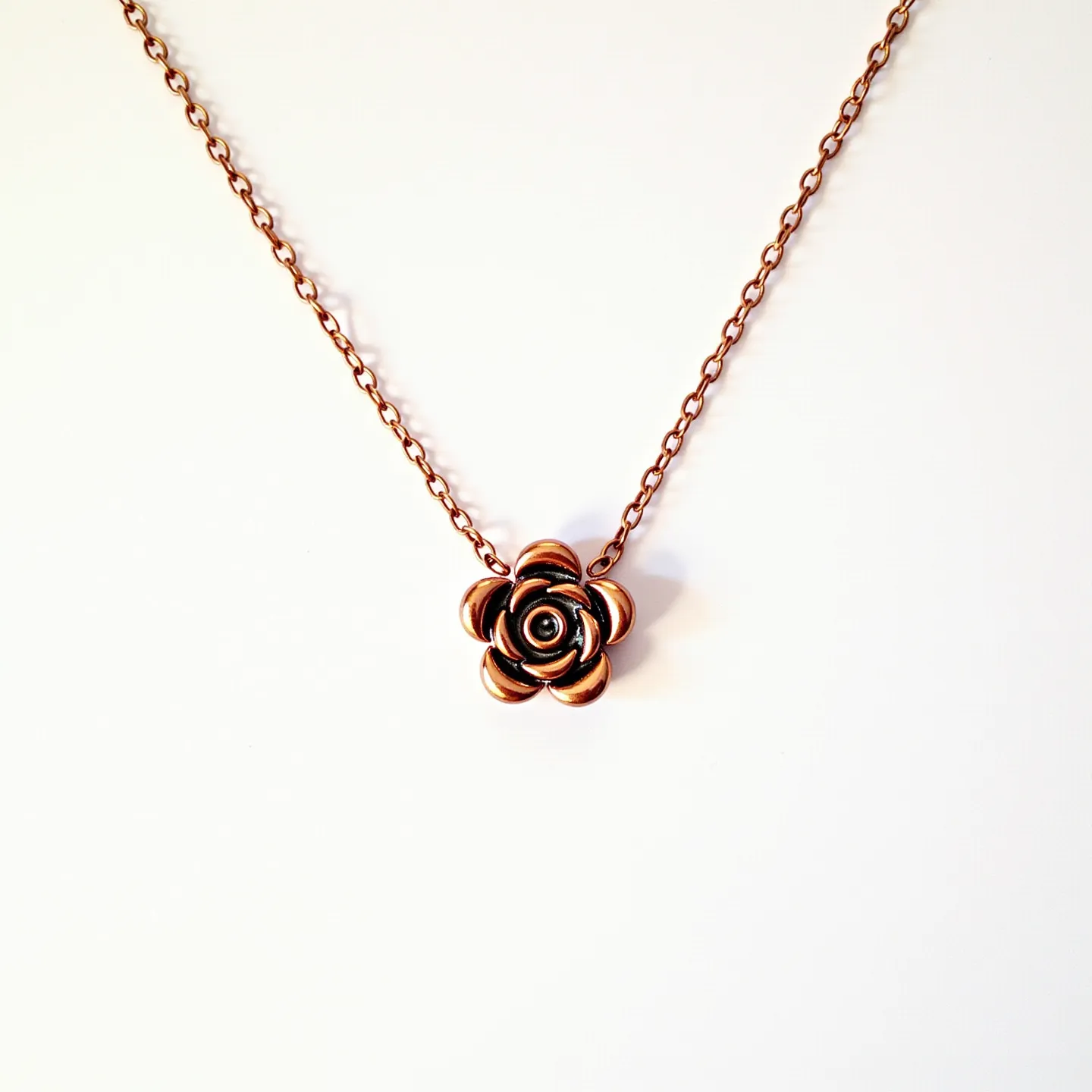 This rose necklace is crafted from bronze-toned metal, forming a delicate rose pendant that hangs from a matching bronze chain. The simplicity of the design emphasizes the intricate detailing of the rose, which is stylized and polished, lending it a classic and elegant appearance. The rose itself does not feature any additional gems or stones, maintaining a cohesive metallic look. The chain links are elegantly proportioned, and the necklace likely includes a standard clasp that complements the overall design, providing both functionality and seamless integration with the piece's aesthetic.