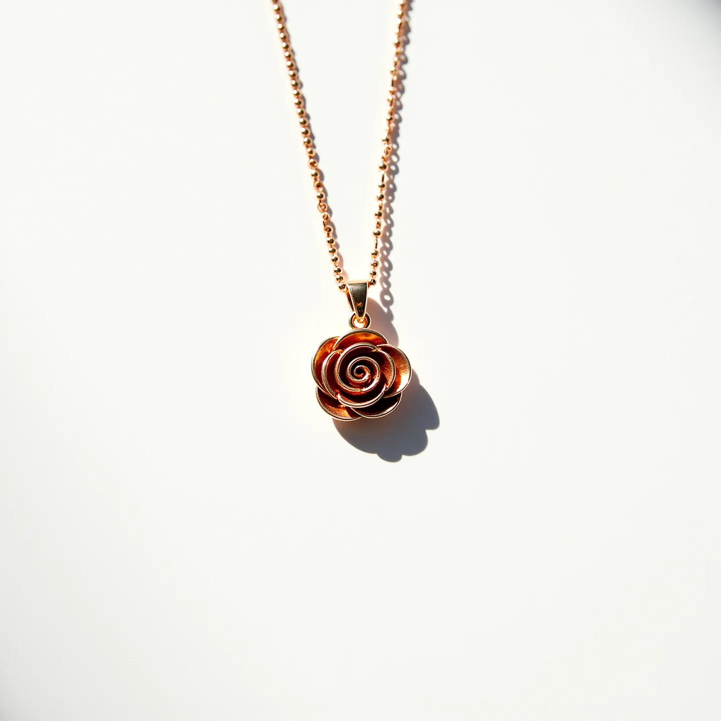 This rose necklace features a stunning rose pendant crafted from metal with a polished, reddish hue that gives it a warm, elegant appearance. The petals are beautifully layered, creating a realistic floral design that captures light effectively. The rose is attached to a fine chain with a classic round link design, providing both durability and a delicate aesthetic. The necklace includes a simple, secure clasp that complements the overall refined style, ensuring that the piece can be worn with ease. The craftsmanship and attention to detail make this necklace a timeless accessory.