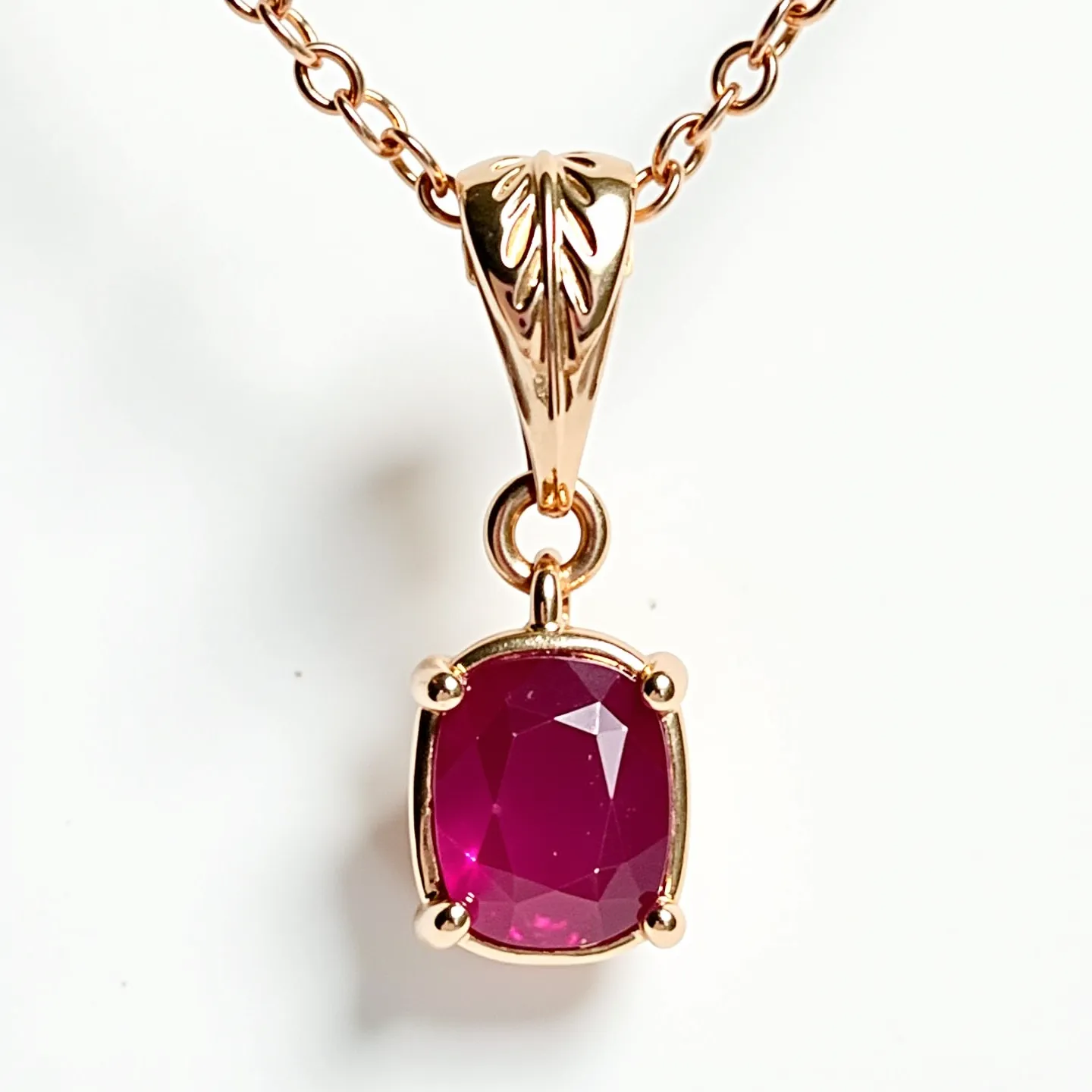 This ruby necklace features a stunning cushion-cut ruby set in a prong setting, crafted to highlight the gem's vibrant red hue. The setting and the chain appear to be made of gold, adding an elegant and complementary warmth to the overall design. The pendant is attached to the chain with an intricately designed loop, which includes a leaf motif, enhancing the necklace's sophisticated aesthetic. The chain is composed of delicate, interlinked loops, providing both durability and a touch of elegance to the piece.