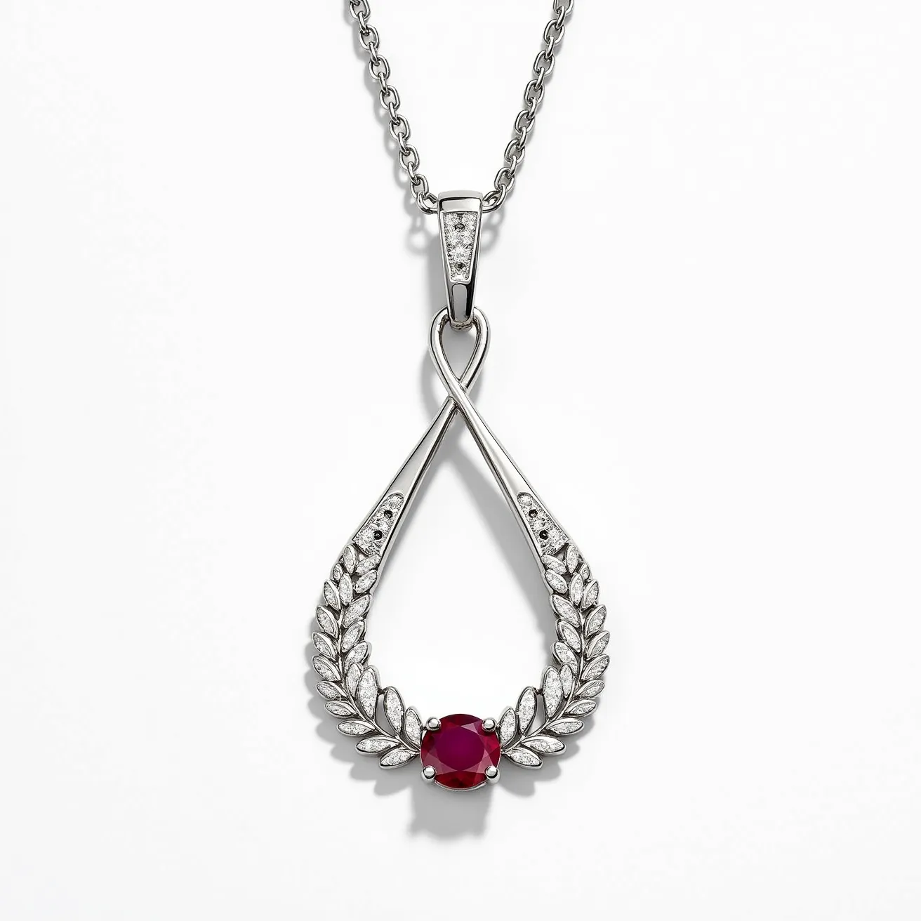 This ruby necklace features a prominent round-cut ruby set at the base of a sophisticated metal framework resembling an ornate laurel wreath. The ruby is held securely by prongs, providing a striking contrast to the intricate setting. The metalwork appears to be a polished silver or white gold, enhancing the vibrant red hue of the ruby. Embedded within the design are small diamonds or diamond-like stones that add a touch of sparkle. The pendant is attached to a delicate chain with a standard clasp, ensuring both security and elegance.