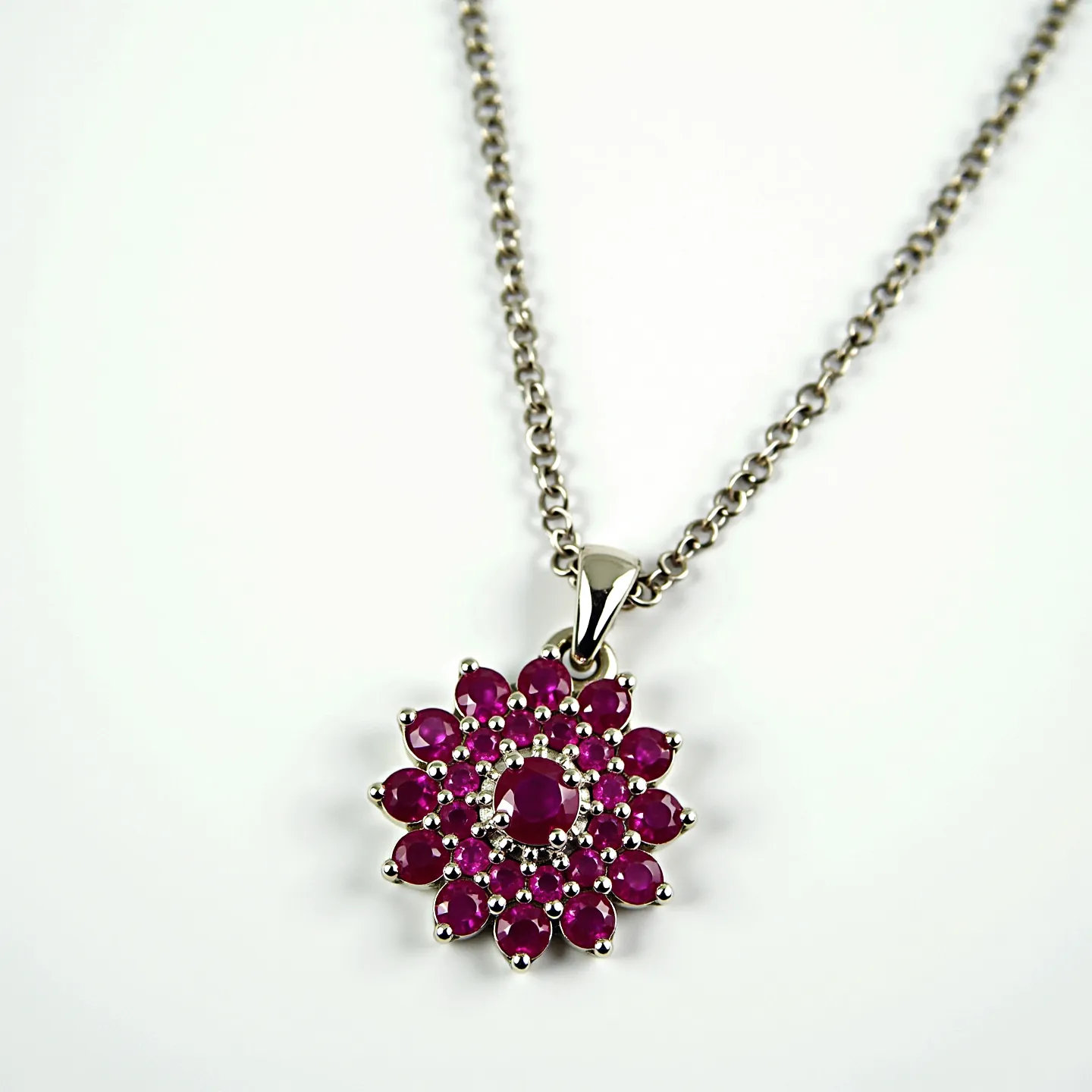 This ruby necklace features a striking arrangement of red rubies set in a decorative floral pattern. The rubies are oval and round cut, creating a vibrant, radiant centerpiece. The stones are set in a prong setting, which elegantly showcases the brilliance and color of each gem. The necklace is crafted with a white metal, likely silver or white gold, that complements the deep red hues of the rubies. It is attached to a chain that appears to be a classic cable design, adding to its timeless elegance. The piece is finished with a secured clasp, ensuring both functionality and style.