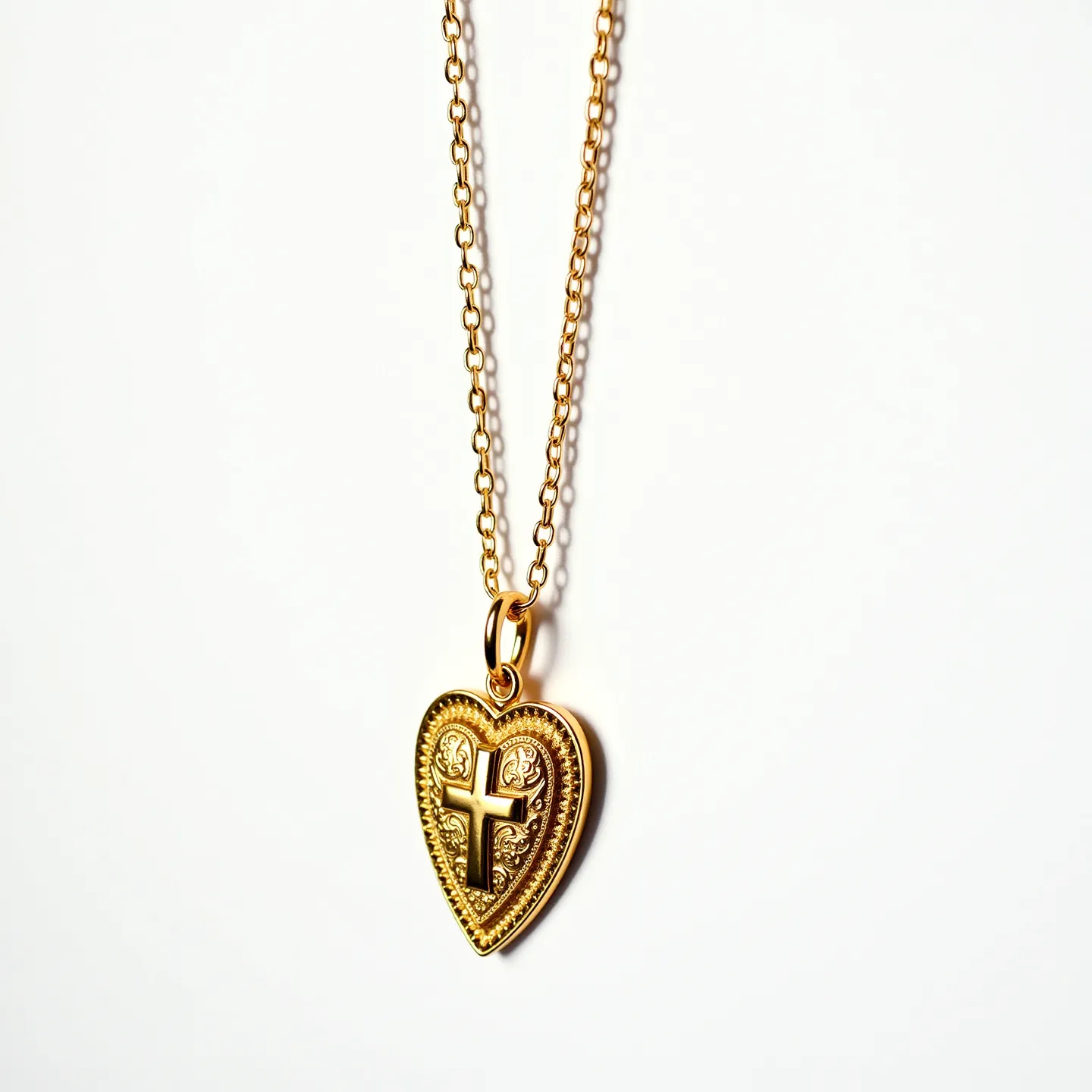 This sacred heart necklace features an intricately designed heart-shaped pendant made of a gold-colored metal. The pendant displays a raised cross motif at its center, surrounded by ornate detailing that enhances its visual appeal. Attached to a fine chain of matching gold hue, the pendant and chain are connected via a simple but elegant loop bail. The necklace incorporates a classic chain link pattern, ensuring a cohesive look. There are no visible gemstones or additional adornments, highlighting the beauty of the design itself. The clasp style is not clearly depicted, but it aligns with the elegant and understated design of the piece.