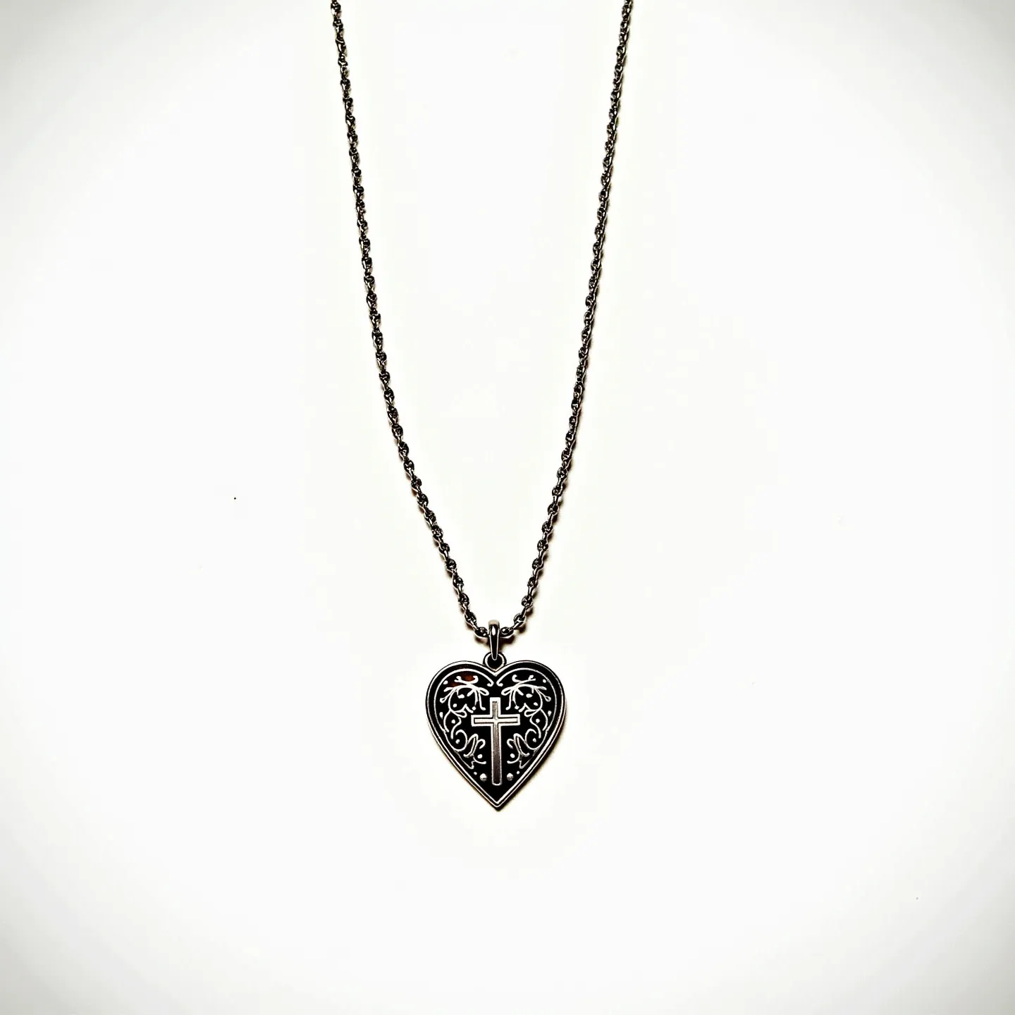 This sacred heart necklace features a heart-shaped pendant intricately designed with a cross motif at its center, surrounded by ornate filigree patterns. The pendant is crafted from a metallic material, likely silver or a similar alloy, giving it a subtly polished appearance. The chain is composed of small, interconnected links that complement the pendant's elegance, likely made of the same material as the pendant for a cohesive look. The attachment is a simple loop through which the chain is threaded, and the necklace likely includes a standard clasp mechanism, such as a lobster or spring ring clasp, for secure closure. The design is both symbolic and aesthetically pleasing, blending religious iconography with decorative artistry.