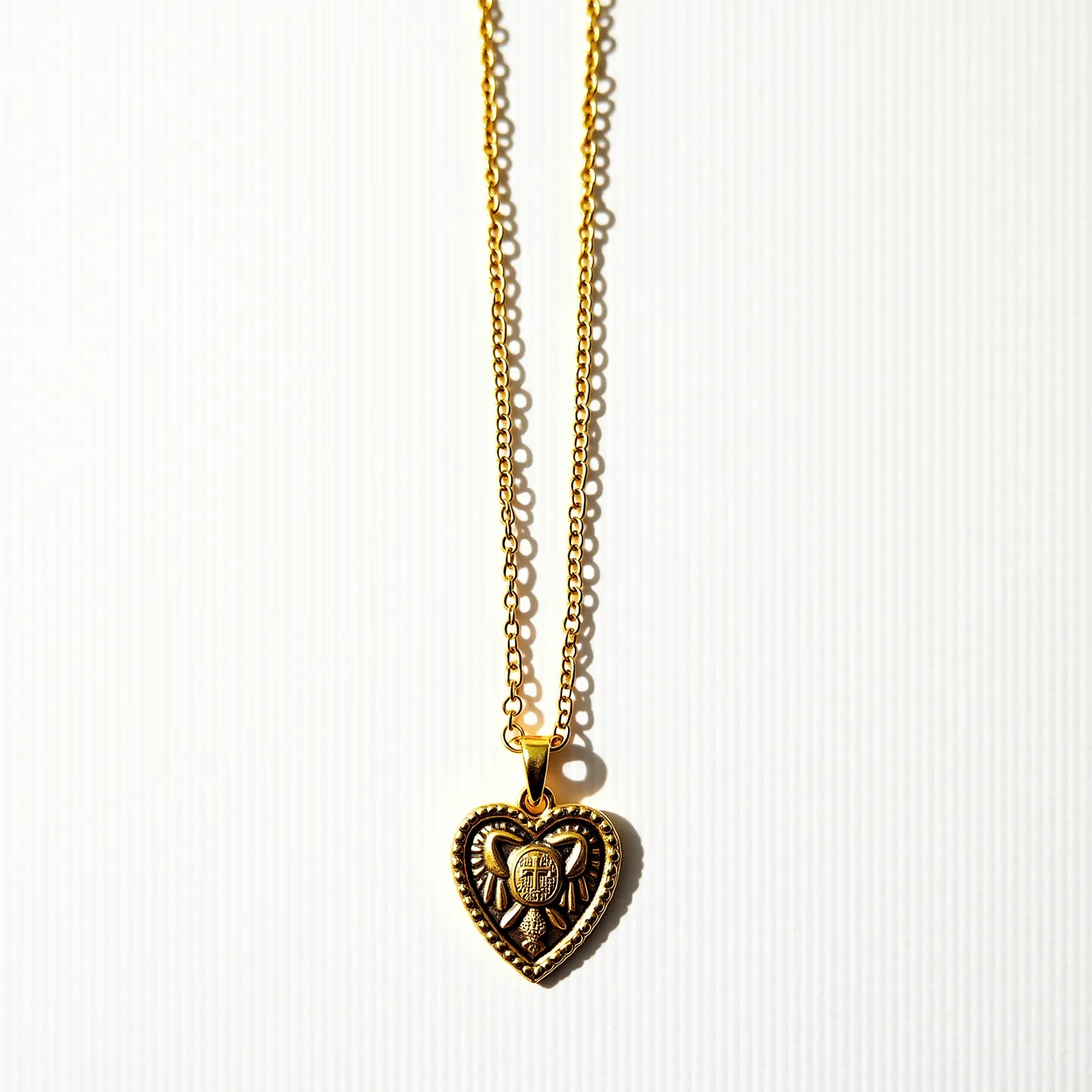 This sacred heart necklace features an intricately designed heart-shaped pendant crafted from metal with a gold hue, possibly gold-toned or gold-plated. The heart pendant is adorned with detailed engravings that emphasize its sacred symbolism, including a border that resembles beading or granulation. The pendant hangs from a delicate double-link chain, also in a matching gold tone, which enhances its elegant and unified appearance. The necklace is secured with a simple yet functional clasp, which is likely a lobster or spring ring style, ensuring ease of wear and security.