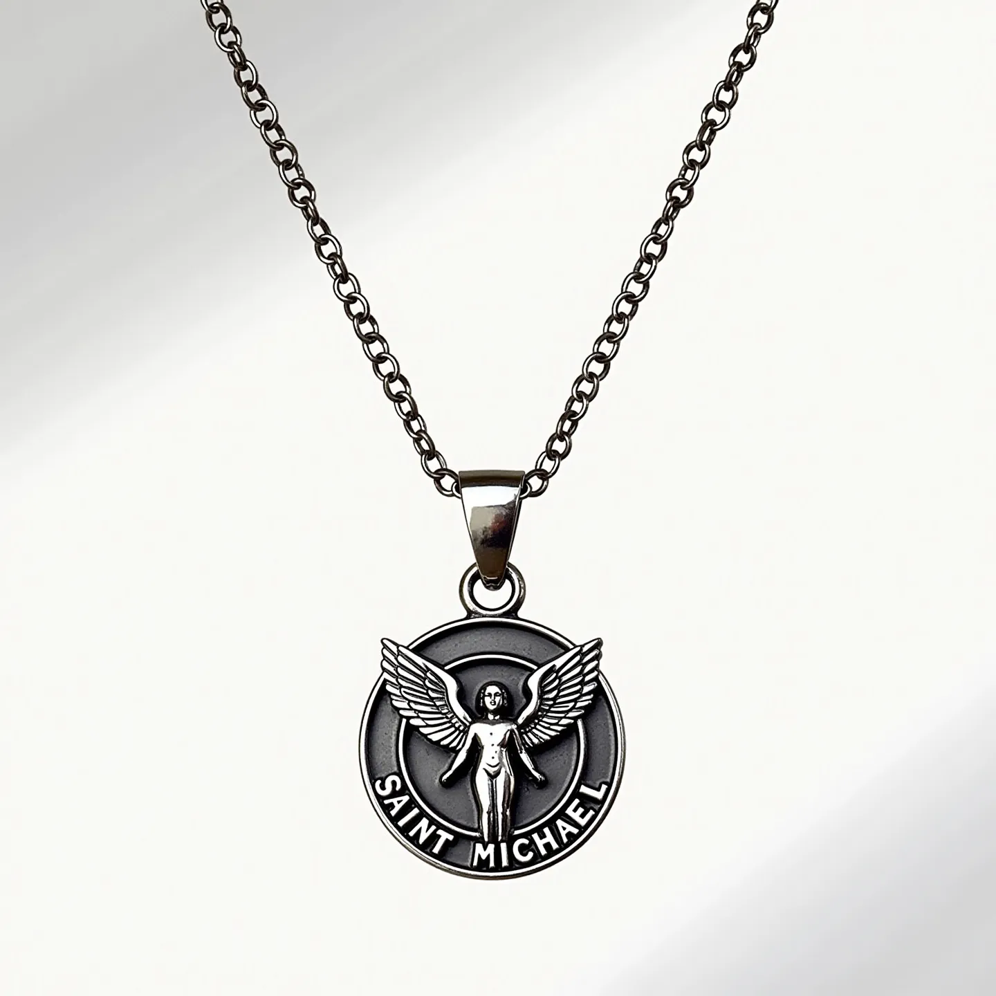 This Saint Michael necklace features a medallion crafted from a dark metallic material, possibly stainless steel or a similar alloy, with a striking depiction of Saint Michael, known for being an archangel. The medallion is round and exhibits intricate detailing of the saint with outstretched wings, encircled by the inscription “SAINT MICHAEL.” The pendant is suspended from a matching dark-colored chain with interlocking links, suggesting durability and a classic aesthetic. The chain appears to have a standard clasp, ensuring secure attachment. There are no visible gems or stones embedded in the medallion, allowing the focus to remain on the engraved imagery and design.