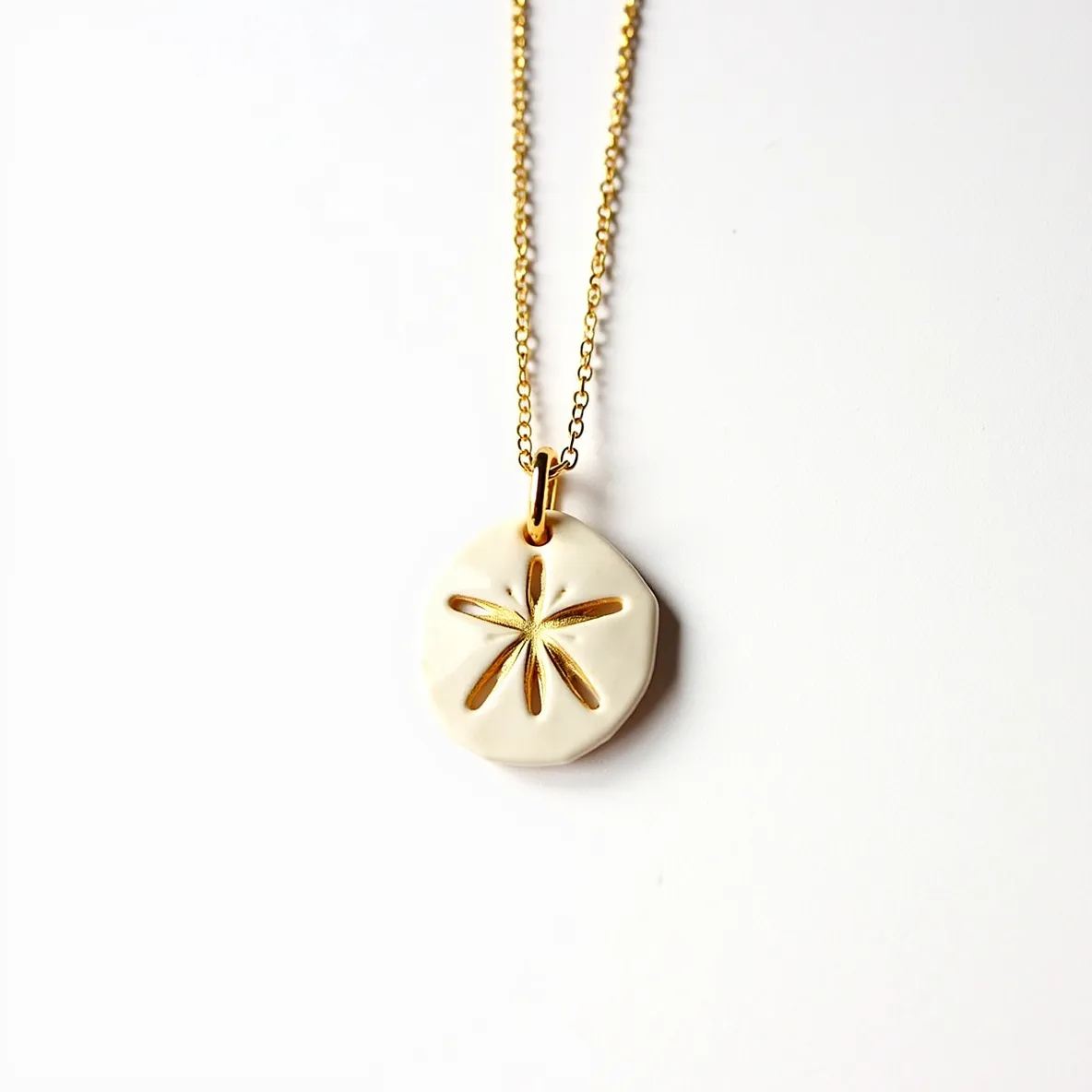 This sand dollar necklace features a pendant shaped like a sand dollar, primarily crafted from a material that appears to mimic the natural texture and color of an actual sand dollar, possibly resin or smooth ceramic. It is accented with gold-toned details that highlight the characteristic star pattern in its center. The pendant is suspended on a delicate gold chain, which complements the gold accents of the pendant. The chain is linked to the pendant with a simple gold loop or bail, allowing it to hang gracefully. The necklace is completed with a standard lobster clasp, securing the piece for wear.