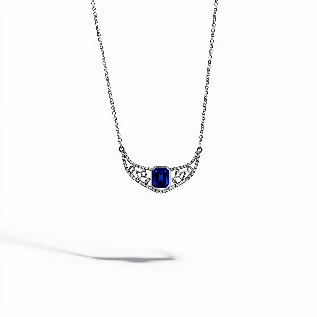 This sapphire necklace features a striking, deep blue, emerald-cut sapphire as its centerpiece. The gemstone is elegantly set in a secure prong setting flanked by an intricate design adorned with numerous small, round-cut diamonds, enhancing the necklace’s luxurious appeal. The base metal appears to be white gold or platinum, complementing the cool tones of the sapphire and diamonds. The necklace is supported by a delicate chain, likely of the same metal, and it includes integrated connections on either side of the decorative section, providing seamless continuity and stability in its design.