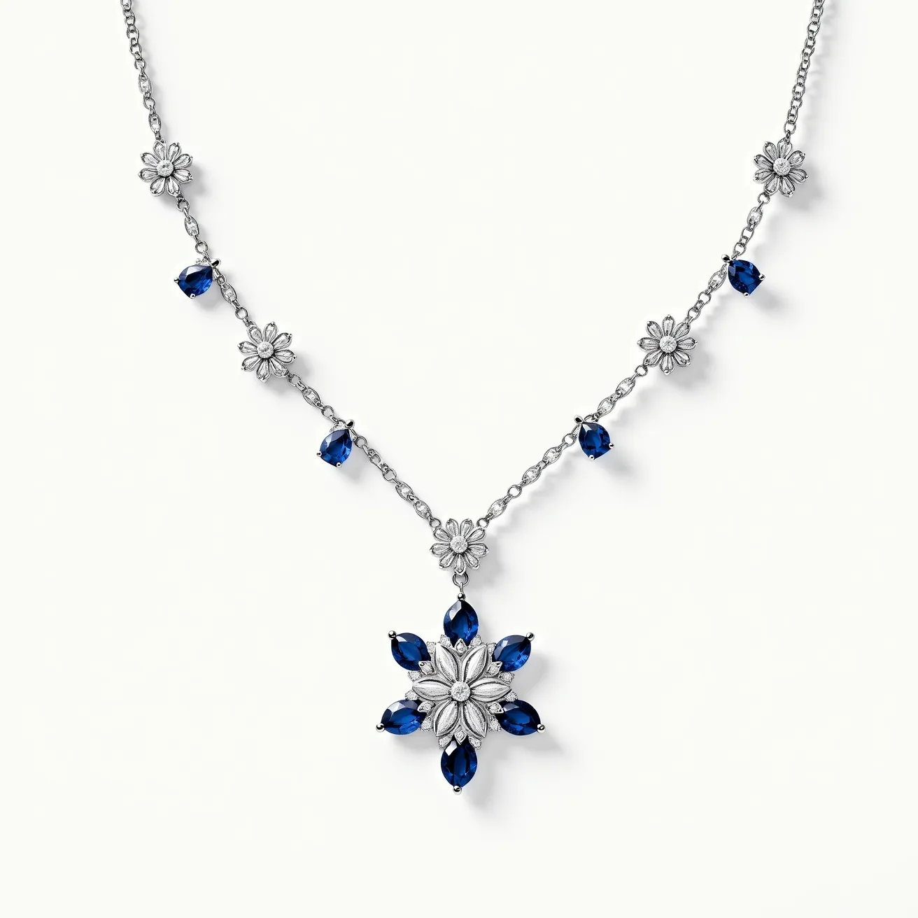 This sapphire necklace features a delicate design with deep blue, teardrop-shaped sapphire stones. The sapphires are set in a symmetrical pattern, showcasing a central flower motif with petals. Each sapphire is held by a secure prong setting, ensuring their stability and prominence. Silver metal links interconnect a series of small, intricately detailed flower accents, consistent throughout the chain, adding elegance to the overall appearance. The pendant, centered on the necklace, mirrors the floral theme with alternating sapphire and silver petal designs, highlighting a central round gem. The necklace likely employs a discreet clasp at the back for secure attachment.