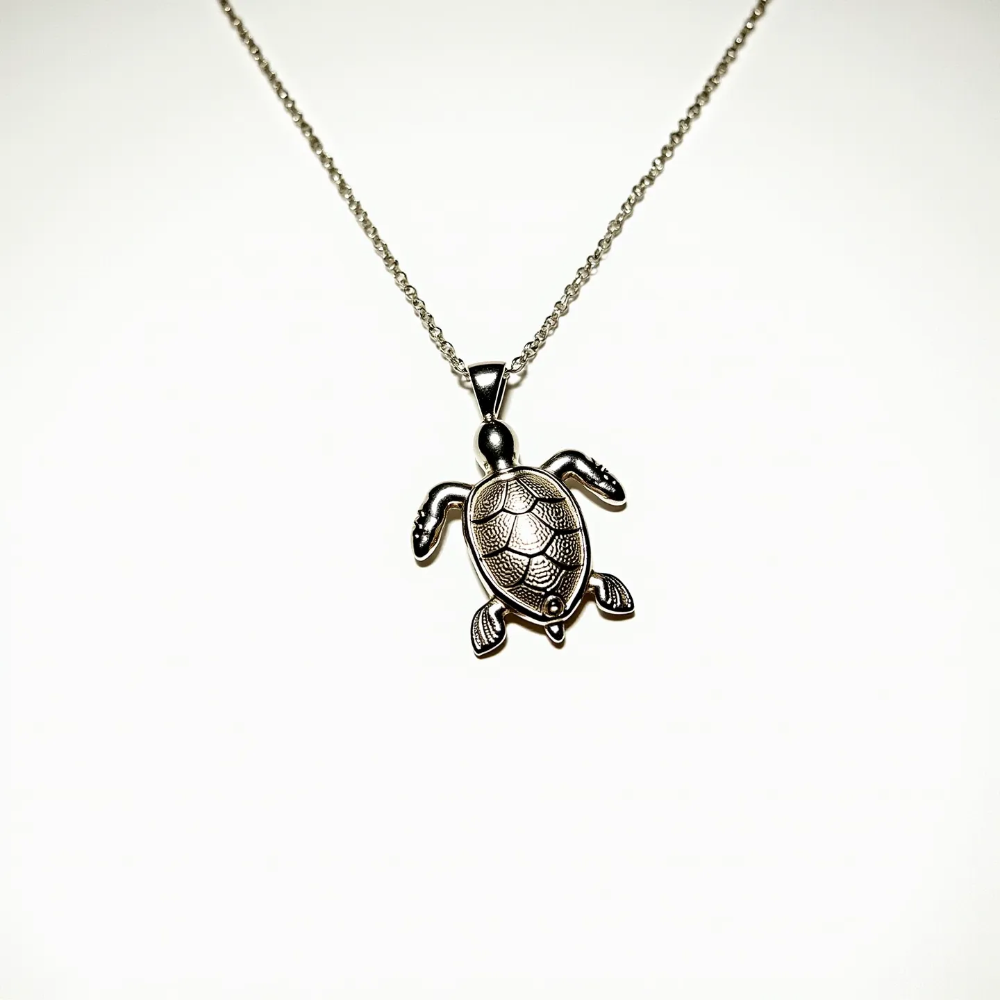 This sea turtle necklace features a pendant crafted from what appears to be a silver-toned metal, intricately shaped and textured to mimic the appearance of a turtle's shell and limbs. The pendant hangs from a delicate chain that is likely made from a similar metal, adding to its cohesive design. The turtle's back is slightly raised and exhibits a detailed pattern typical of a natural turtle shell. There are no visible gems or stones embedded in the pendant. The necklace is equipped with a simple, triangular bail that securely attaches the pendant to the chain, allowing it to hang gracefully. The overall design is sleek and elegant, making it a versatile accessory.