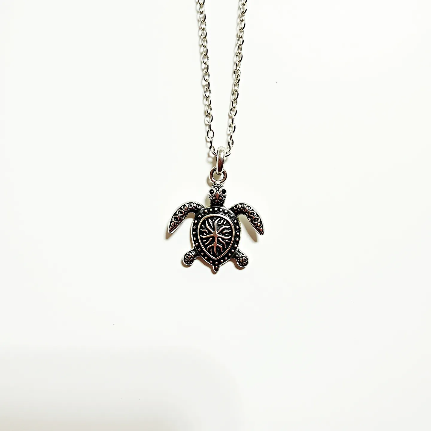 This sea turtle necklace features a pendant crafted with a metallic material, likely silver or a silver-toned alloy, highlighted with intricate detailing on the shell to resemble a natural pattern. The turtle's limbs and head are accentuated with raised circular designs, adding texture and depth to the charm. The pendant is suspended from a simple, linked chain that matches the metallic hue of the turtle. The attachment is facilitated by a small loop integrated into the pendant, allowing smooth movement along the chain. The clasp is a typical lobster clasp, ensuring secure fastening and ease of use.