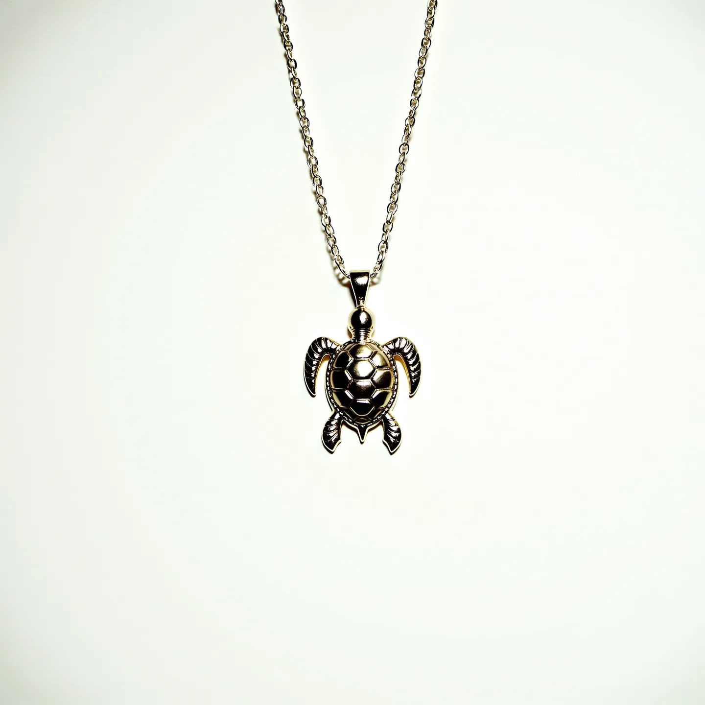 This sea turtle necklace features a pendant crafted from metal, showcasing intricate detailing to mimic the shell and limbs of a sea turtle. The pendant hangs from a chain with small, evenly spaced links, likely made of the same metal or a complementary one, providing a consistent and harmonious appearance. The turtle shell’s design incorporates a pattern that resembles hexagonal shapes, adding texture and visual interest. The pendant is attached to the chain via a polished metal bail, ensuring it hangs securely and aligns evenly. The necklace's chain is fitted with a standard clasp, commonly used for ease of wear and removal.