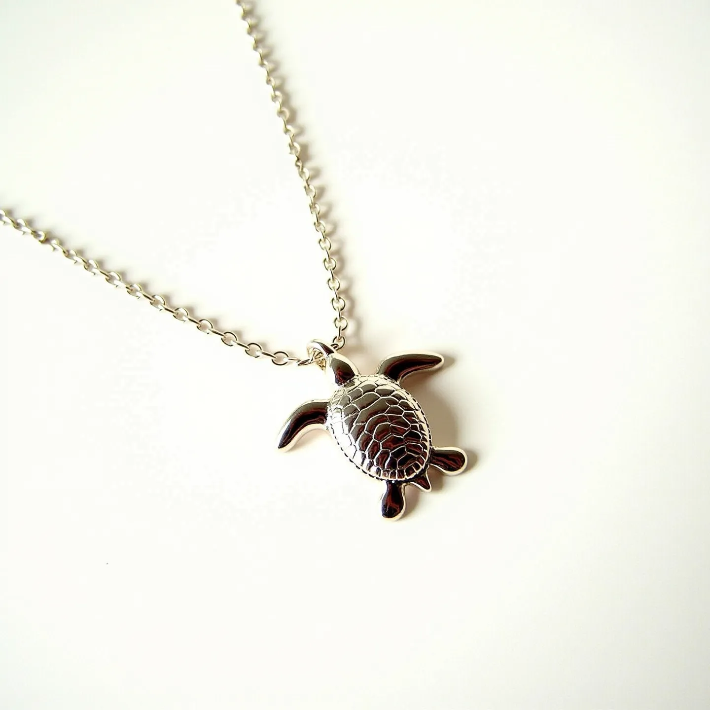 This sea turtle necklace features a pendant shaped like a sea turtle, crafted from a polished silver-colored metal that captures light beautifully across its textured shell. The pendant is attached to a matching chain that appears to be composed of small, uniform links, providing a delicate yet sturdy connection. The chain seems to include a simple clasp mechanism, ensuring both security and ease of use.