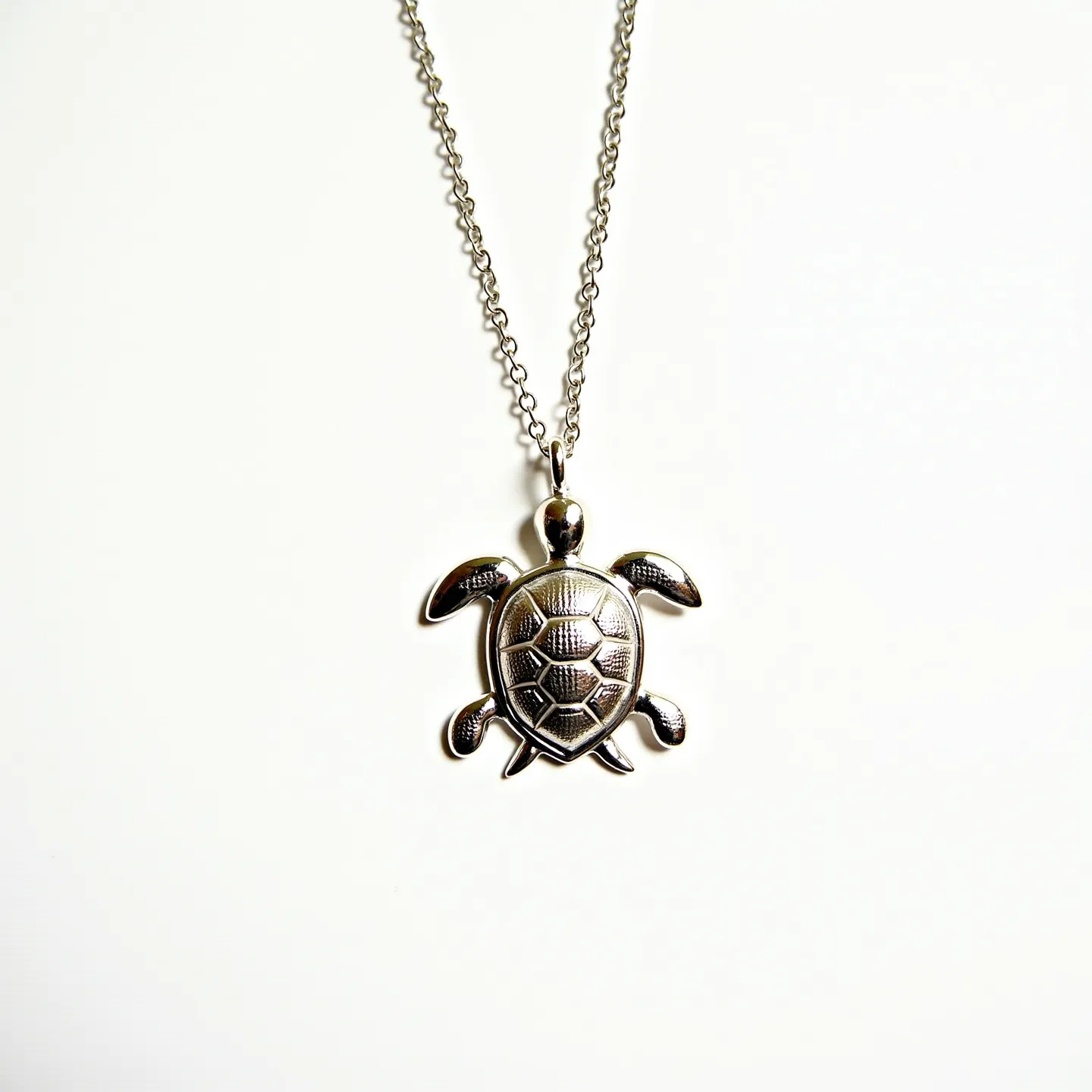 This sea turtle necklace features a finely crafted pendant in the shape of a turtle, intricately designed to showcase detailed patterning on its shell. Made from a metallic material, the pendant exhibits a polished silvery sheen. The pendant is suspended from a delicate chain that appears to be composed of similar metal, adding continuity to the piece. No visible gems or stones are incorporated into the design, and the necklace includes a standard chain clasp for secure fastening. The overall design captures a marine aesthetic, appealing to nature enthusiasts and adding a touch of elegance to casual wear.