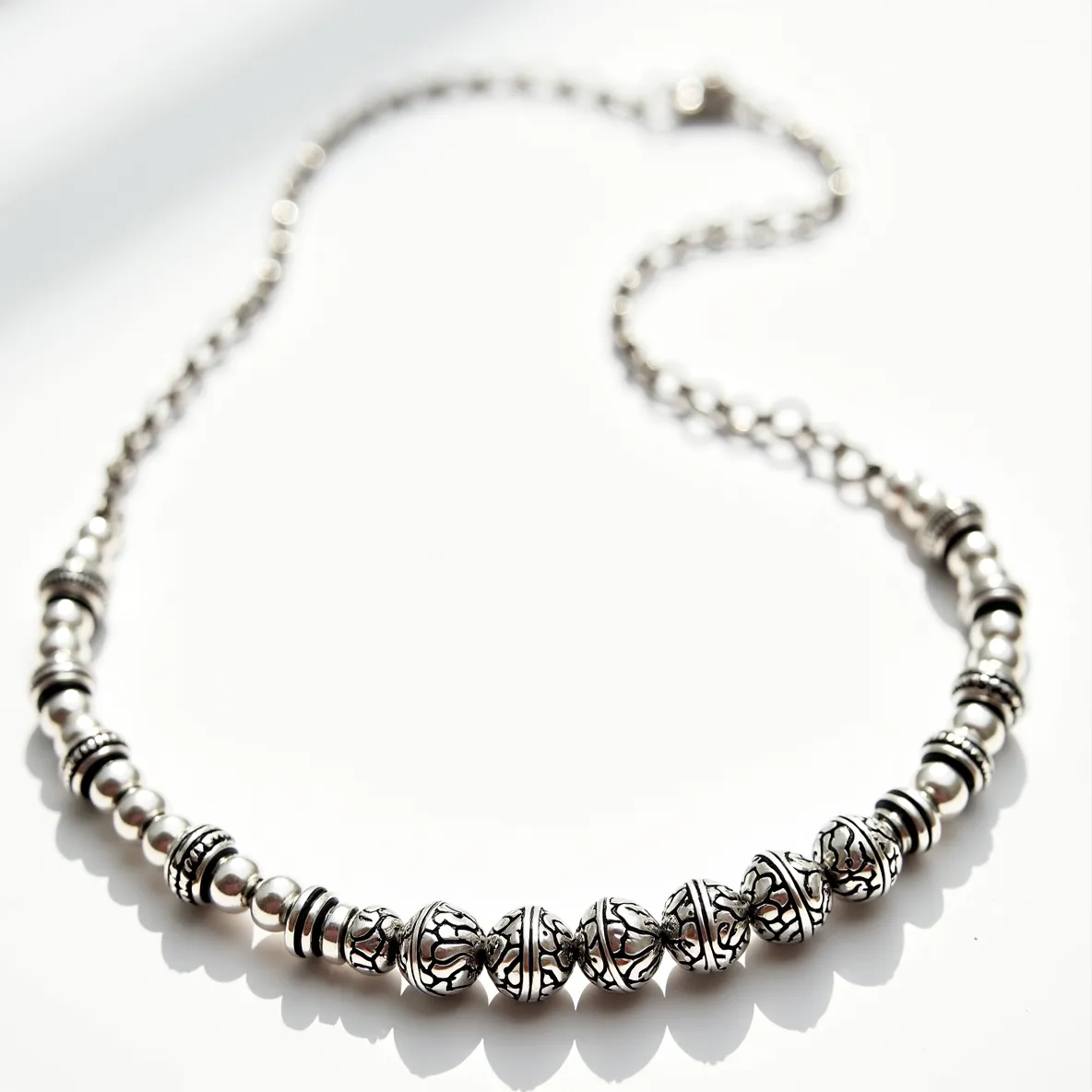 This silver bead necklace features an elegant arrangement of intricately designed silver beads with varied patterns and textures, showcasing a mix of smooth and detailed motifs. The beads are polished to a bright sheen, highlighting the artistry of the craftsmanship. Interspersed among the beads are ornate spacer beads that enhance the overall design. The necklace is completed with a robust clasp that ensures secure fastening, making it both a stylish and practical accessory for any occasion.