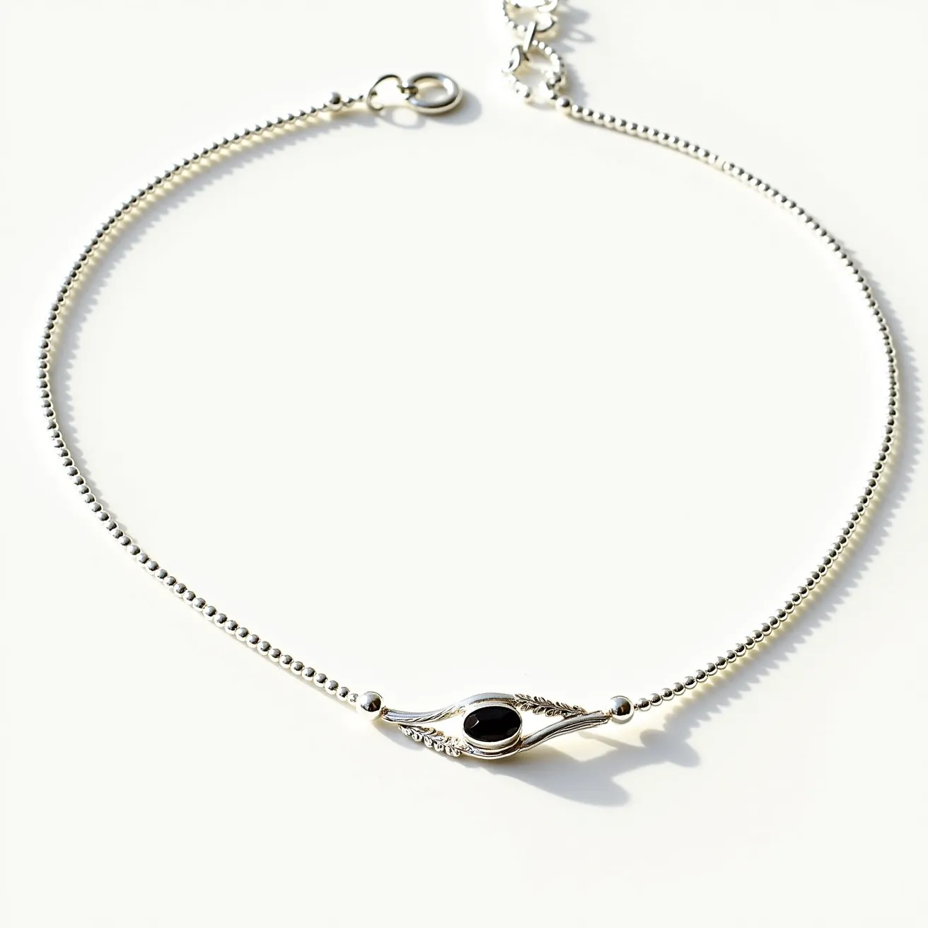 This silver bead necklace features a delicate arrangement of small, round silver beads that form a graceful chain. At the center, there is a striking black gemstone, likely an onyx, which is oval in shape and set in a bezel setting. The design around the gem includes intricate silverwork that resembles leaves or feathers, enhancing its elegant appearance. The necklace secures with a classic spring ring clasp, ensuring both functionality and a seamless aesthetic.