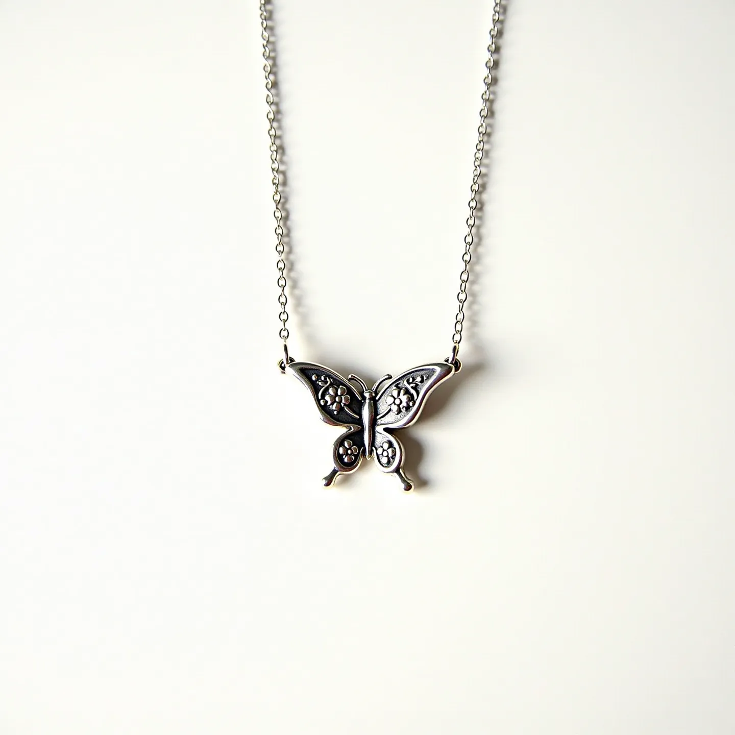 This silver butterfly necklace features a detailed butterfly pendant crafted from silver, showcasing intricate patterns on its wings that add texture and visual interest. The butterfly is set on a delicate silver chain, which enhances its elegant appearance. The pendant includes small circular design elements that could resemble gemstones, though their specifics are unclear from the image. The necklace is likely secured with a standard clasp, typical for necklaces of this style, which ensures ease of wear and security. Overall, the design combines simplicity with a touch of whimsy, making it a versatile accessory.