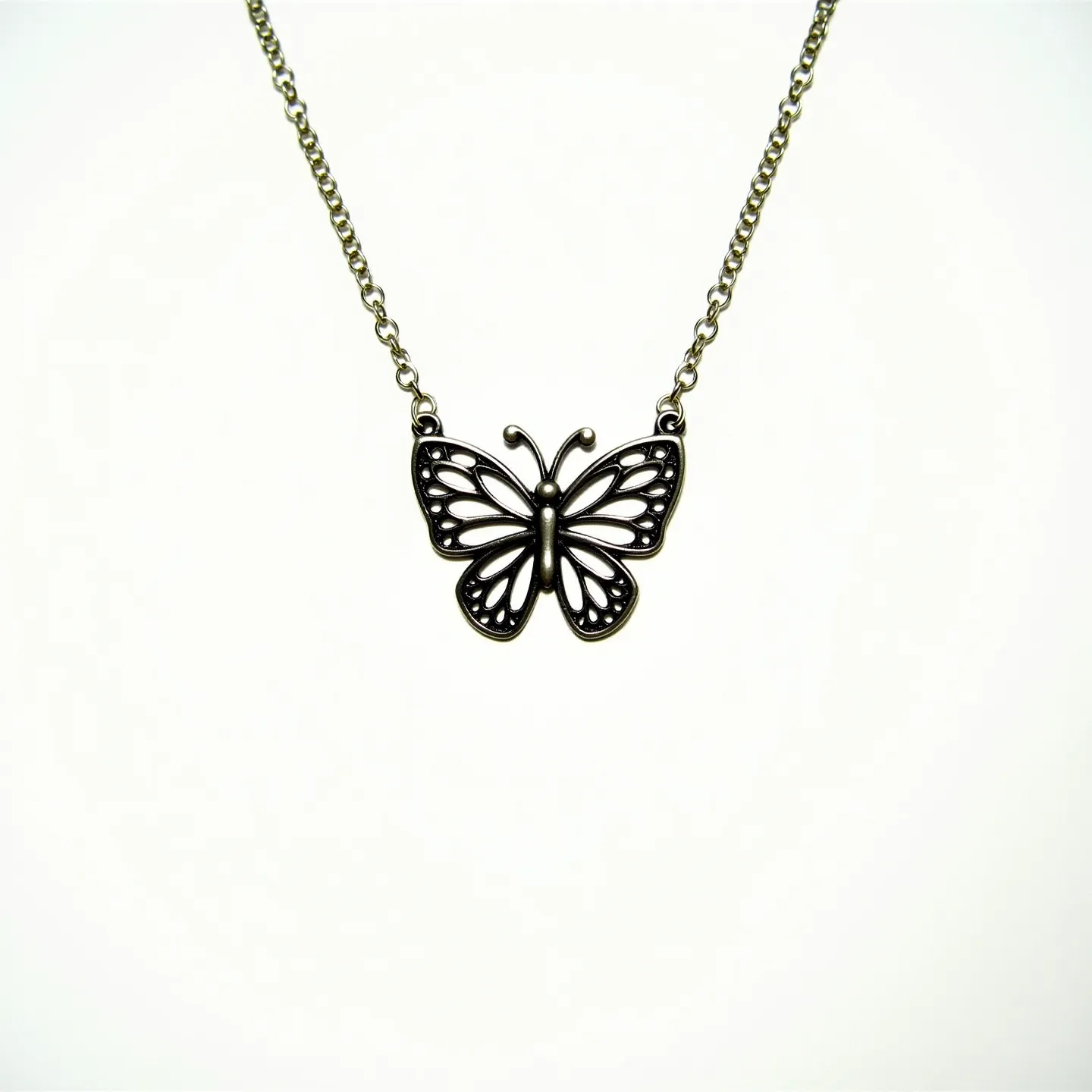 This silver butterfly necklace features an intricately designed butterfly pendant crafted from silver, showcasing a detailed cutout pattern that highlights the delicate wings and antennae. The pendant is connected to a fine silver chain, which complements the elegance of the piece. The chain links are uniform, suggesting a strong yet refined design. The necklace likely includes a standard clasp for secure attachment, ensuring ease of wear. The overall aesthetic is a blend of sophistication and charm, with the silver material providing a classic and timeless appeal.