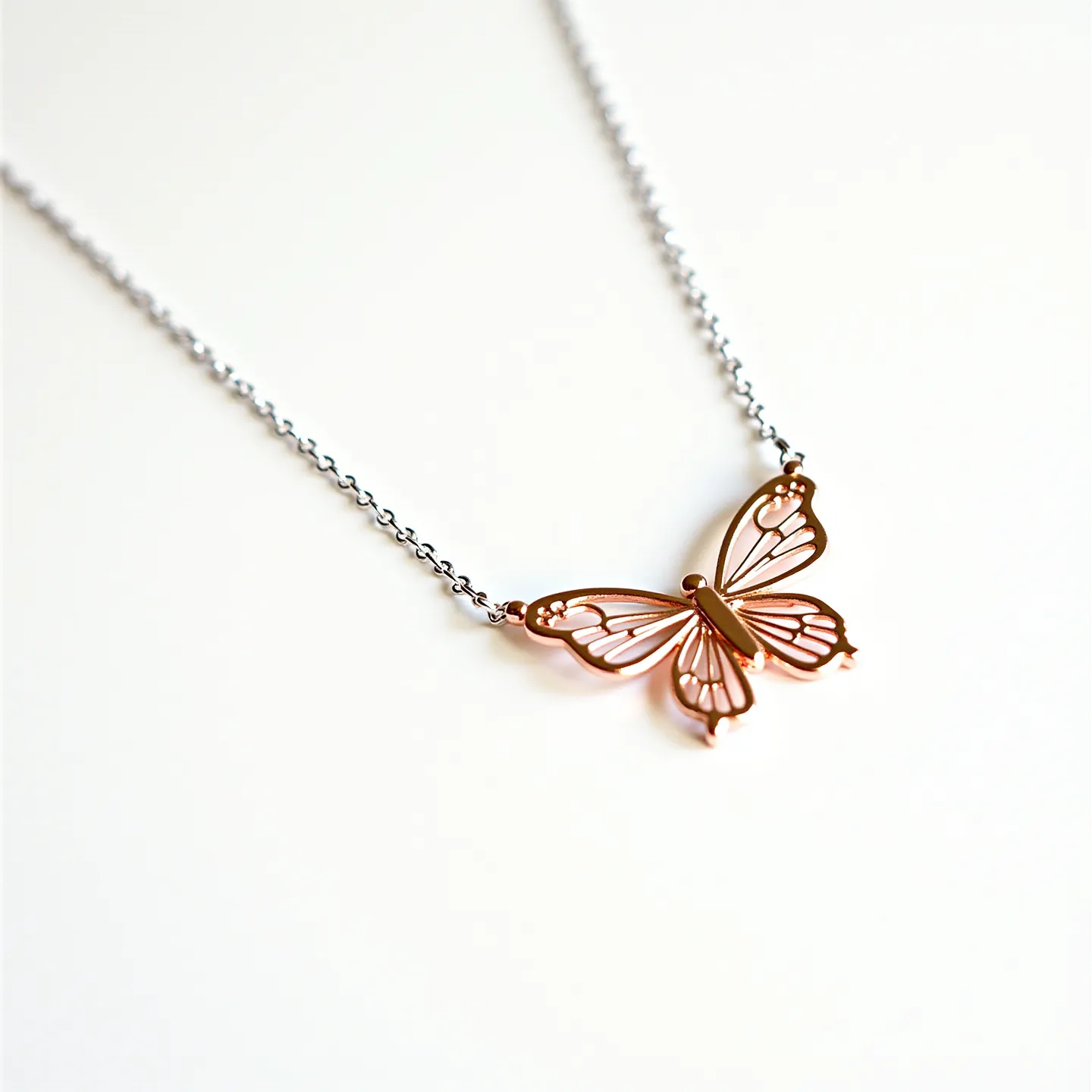 This silver butterfly necklace features a delicate chain crafted from sterling silver, supporting a detailed butterfly pendant. The pendant is composed of intricately cut metal, likely silver-plated or rose gold-toned, designed to resemble the delicate wings and body of a butterfly. The cut-out design highlights the craftsmanship, allowing light to pass through its ornate shapes. While no gemstone accents are evident on this piece, its simplicity and elegance are showcased through the airy and open framework of the butterfly. The necklace is likely secured with a standard clasp attachment, ensuring ease of wear.

