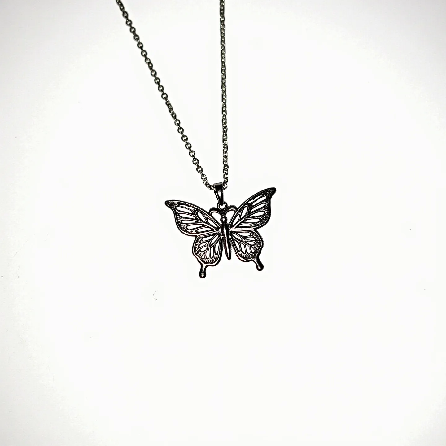 This silver butterfly necklace features a delicate pendant meticulously crafted from silver, showcasing an intricate butterfly design with filigree details that create a sense of lightness and elegance. The pendant hangs gracefully from a fine chain, which is likely also made of silver, ensuring continuity and elegance throughout the piece. The necklace is completed with a standard lobster clasp, offering both security and ease of wear. The overall design highlights the charm and sophistication of the butterfly motif, making it a versatile accessory suitable for various occasions.