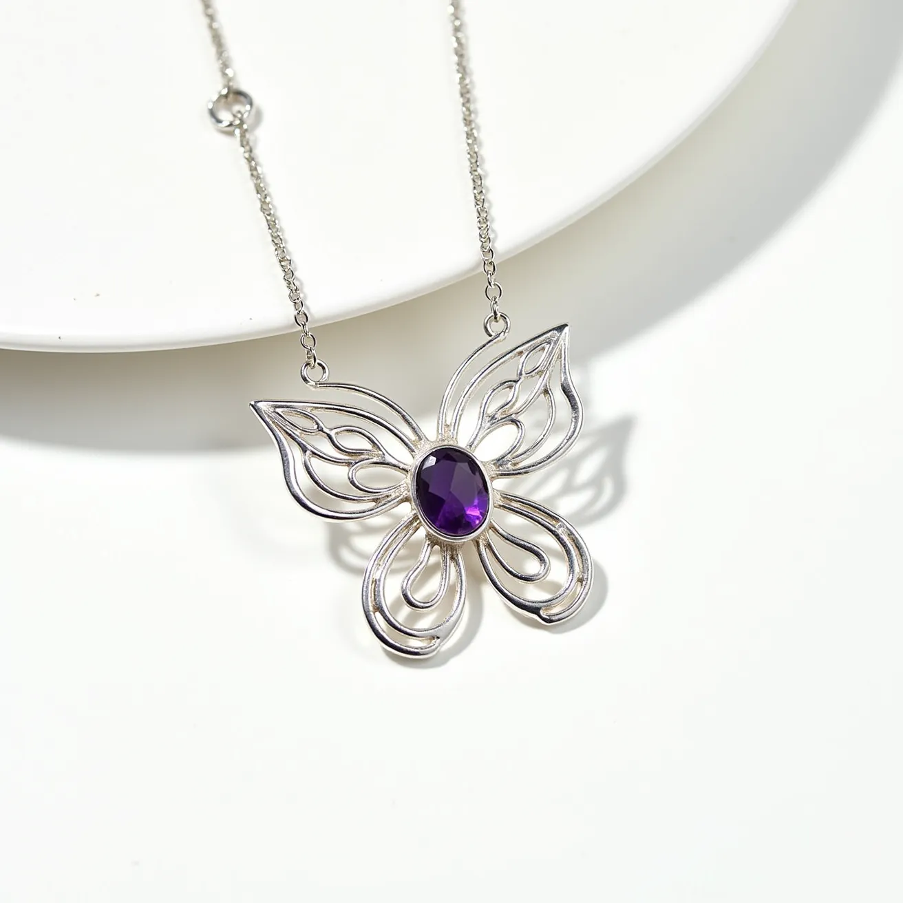 This silver butterfly necklace features an intricate, openwork design crafted from sterling silver, forming an elegant butterfly shape. At the center of the butterfly, there is a prominent, oval-cut purple gemstone set in a bezel setting, which adds a touch of color and sophistication. The necklace is attached to a delicate silver chain, which includes a simple ring clasp for secure fastening. The overall design is both elegant and whimsical, making it a versatile piece for various occasions.