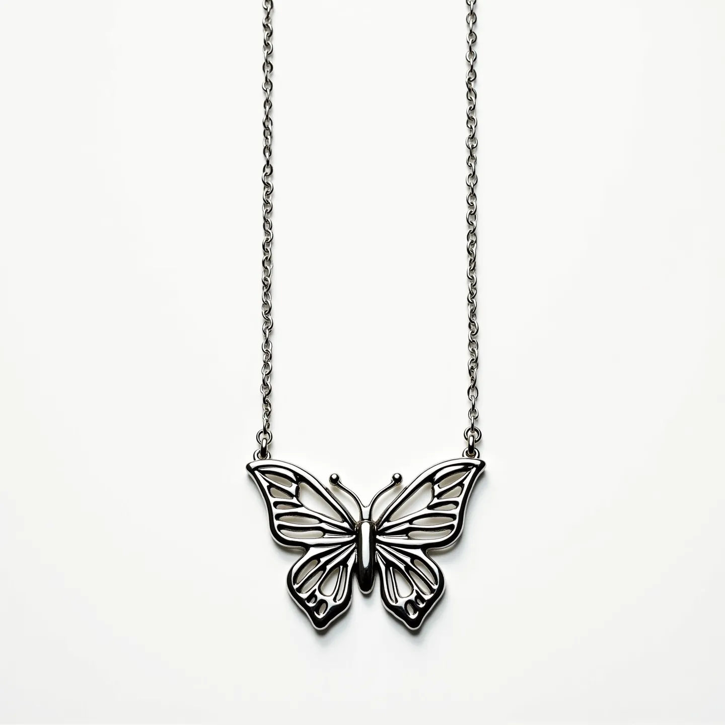 This silver butterfly necklace features a delicately crafted butterfly pendant with intricate cut-out patterns, highlighting the elegance of the design. The necklace appears to be made entirely of silver, showcasing a smooth and polished finish that enhances its sophisticated appearance. The butterfly pendant is securely attached to a fine chain, which is likely connected with a standard spring ring clasp, providing both style and functionality. The absence of visible stones or gems suggests a minimalist and timeless design, focusing on the intricate metalwork of the butterfly motif.