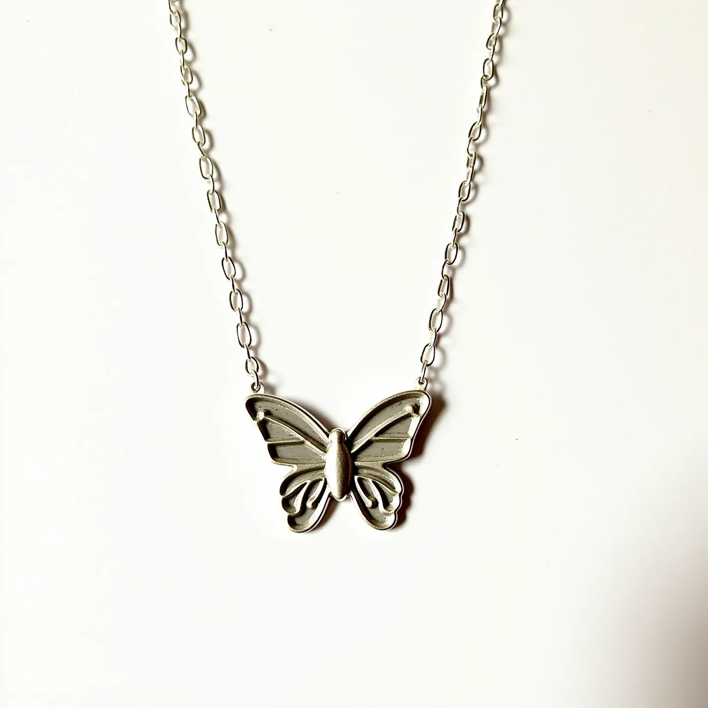 This silver butterfly necklace features a delicate pendant crafted from lustrous silver, intricately designed to resemble a butterfly with detailed wings. The butterfly is elegantly suspended on a silver chain that complements the pendant's reflective finish. The chain appears to have an interlocking link design, providing both durability and flexibility. No visible gemstones are embedded in the pendant, emphasizing the simplicity and elegance of the silver craftsmanship. The necklace likely includes a standard clasp mechanism, ensuring secure wear while maintaining the overall sleek aesthetic.