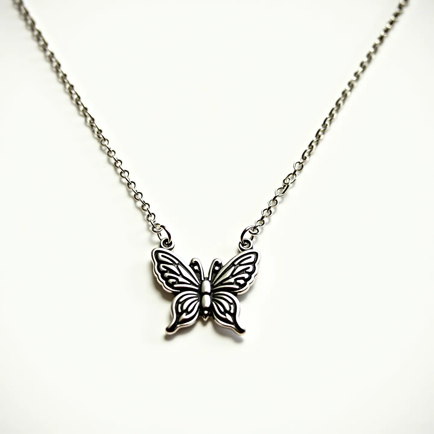 This silver butterfly necklace features an intricately designed butterfly pendant made of silver, showcasing fine detailing on its wings that create an elegant and intricate pattern. The necklace is suspended from a delicate silver chain, connecting to the pendant via small loops on either side of the butterfly's upper wings. The chain likely includes a standard clasp attachment for easy fastening and secure wear. The overall aesthetic of the necklace conveys a sense of delicate beauty and timeless charm without any additional gemstones or embellishments.