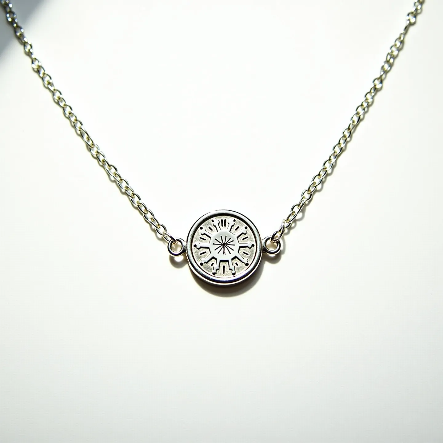 This silver chain features a finely detailed central pendant, crafted from silver, with intricate, engraved patterns radiating from the center in a symmetrical design. The chain is composed of uniform, small links, providing a delicate yet durable appearance. Each end of the pendant is securely connected to the chain with small, round loops, ensuring the centerpiece remains prominently displayed. The chain appears to have a simple and functional clasp, facilitating ease of wear without detracting from its elegant design. This subtle yet striking piece exemplifies craftsmanship in its detailed etching and seamless integration of the pendant with the chain.