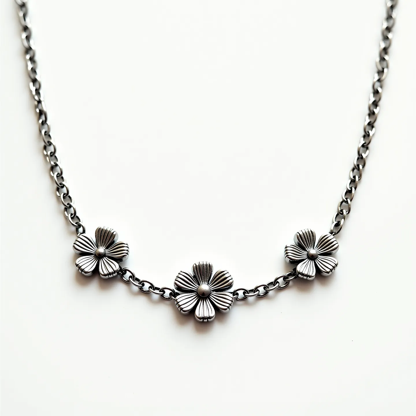 This silver chain features a series of intricate floral designs that are smoothly integrated into its structure. The chain itself is composed of tightly linked, polished silver links that provide durability and a classic aesthetic. The floral motifs are crafted with detailed petal engravings, each centered with a small, rounded metallic bead, adding a touch of elegance and sophistication. The absence of gemstones highlights the purity and sheen of the silver craftsmanship. At its end, the chain likely incorporates a standard clasp, though specifics on its type are not discernible, ensuring the piece can be securely fastened when worn.