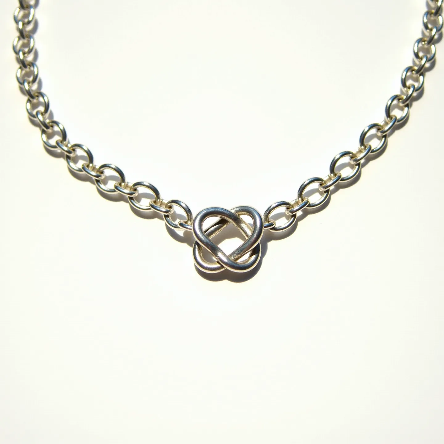 This silver chain features polished, interconnected links, giving it a classic and elegant appearance. At the center, a distinct knot design serves as a focal point, providing a touch of sophistication. The materials appear to be high-quality silver, enhancing its sleek and shiny finish. The chain likely includes a standard clasp mechanism, ensuring secure wear, though the specific type is not visible. The arrangement and craftsmanship suggest a piece suited for both casual and formal occasions, highlighting its versatility and timeless appeal.