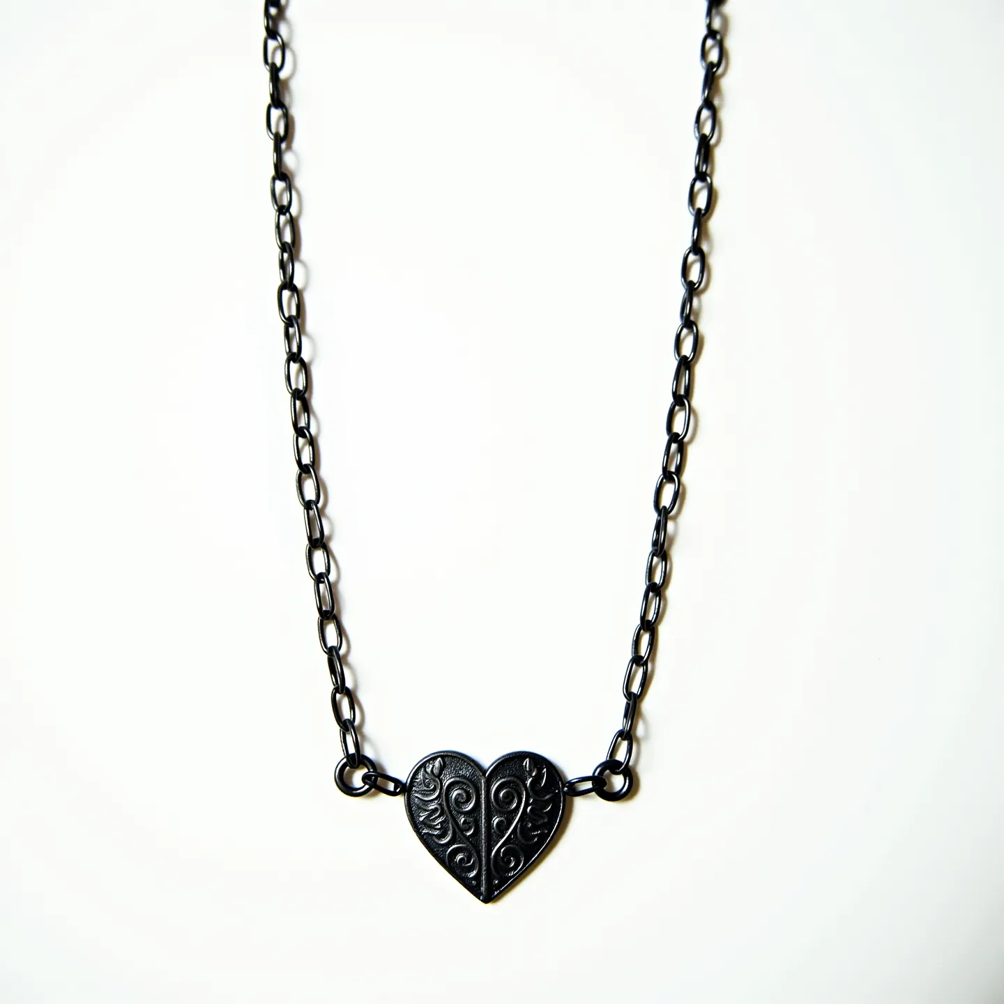 This silver chain features a linked design with a prominent heart-shaped pendant as its centerpiece. The pendant is intricately engraved with swirling patterns, enhancing its ornate appearance. The chain itself appears to have a lobster clasp, ensuring secure attachment and easy wearability. The simplicity of the chain links draws attention to the detailed artistry of the heart pendant, making it a standout piece in the overall design. There is no additional embellishment such as gemstones on this piece, allowing the engraved heart to serve as the focal point.